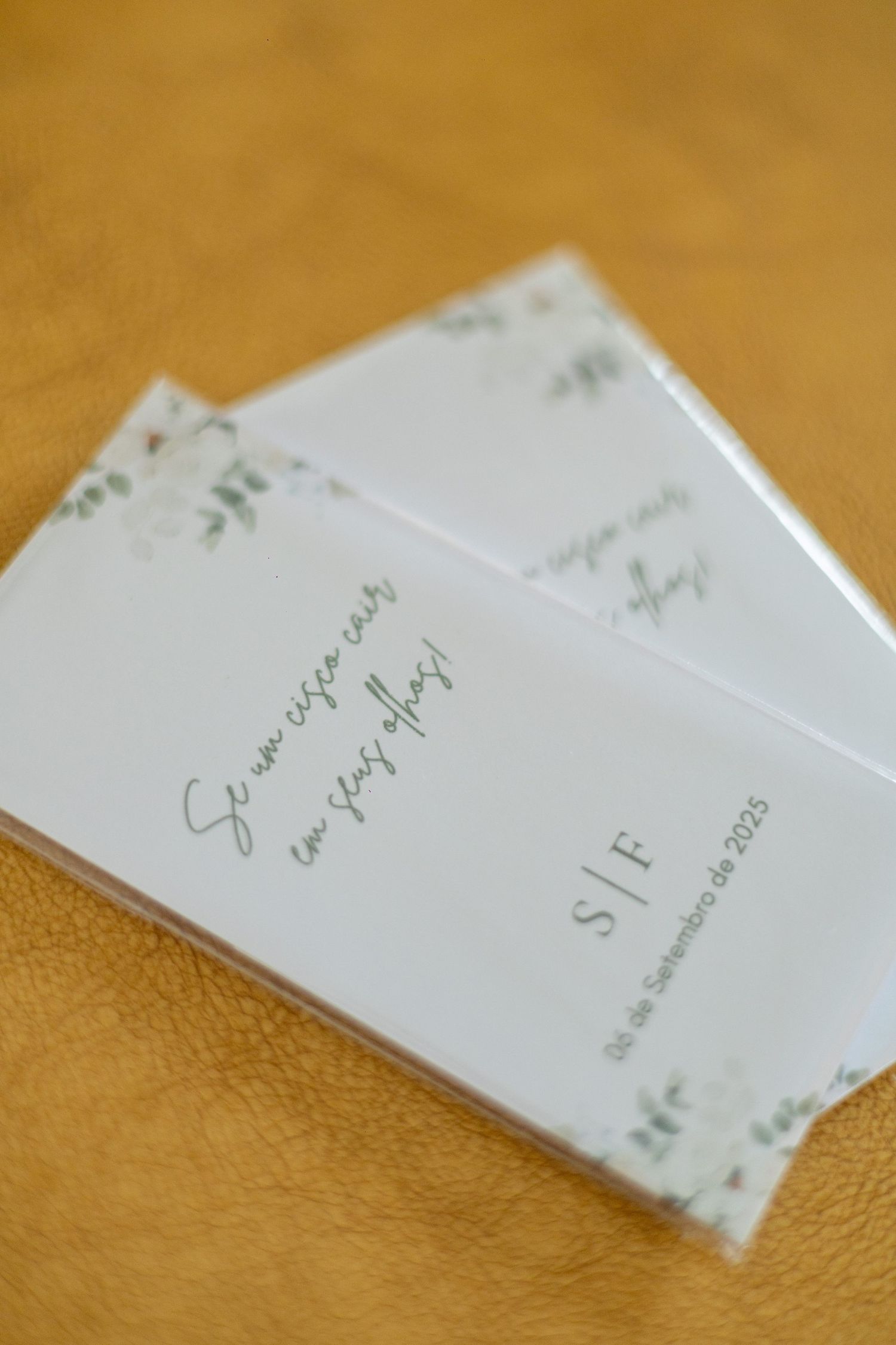 Two elegant white wedding invitation cards with green botanical accents and monogram S|F on a golden background.