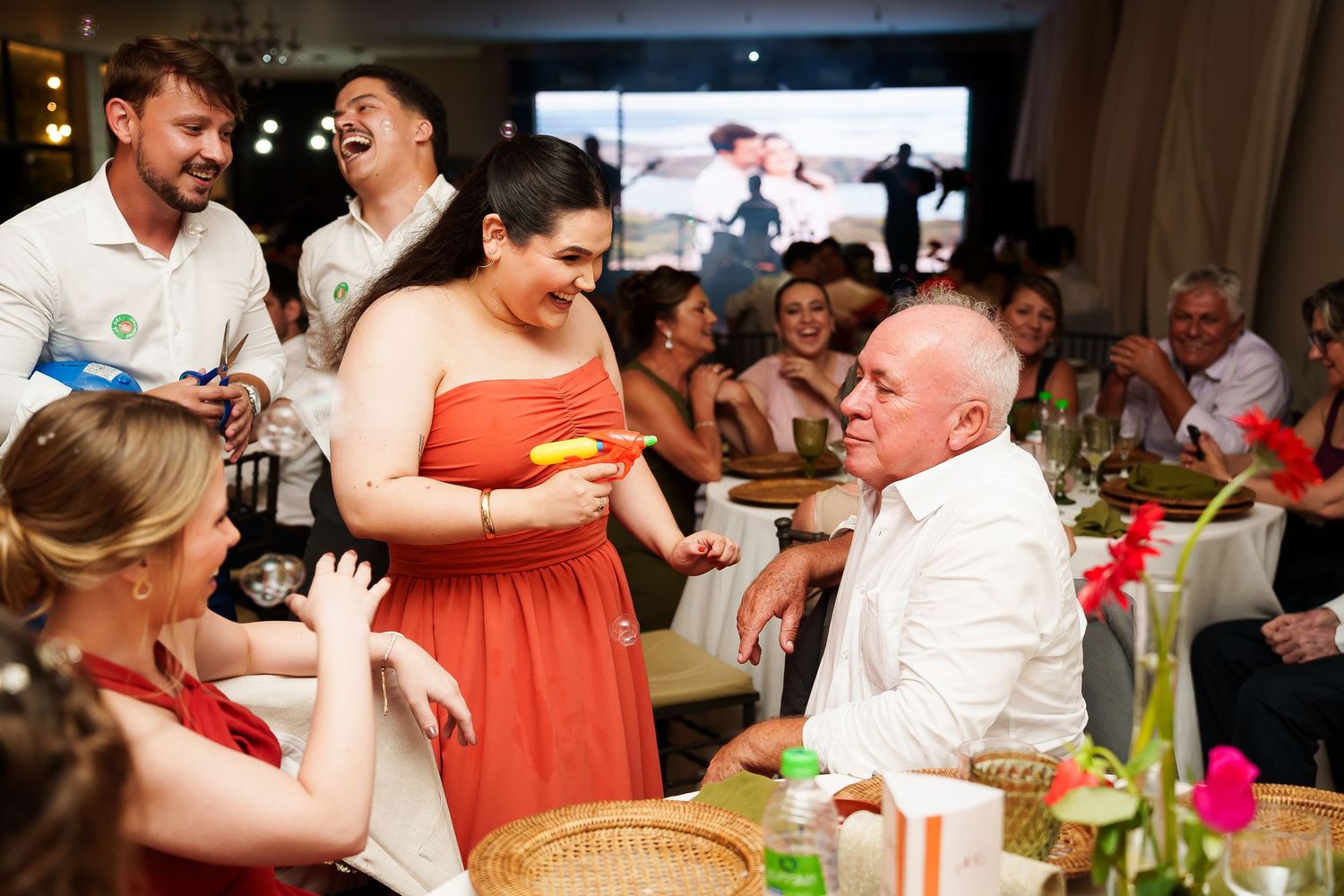 Guests laughing and celebrating at a festive wedding reception dinner party indoors.