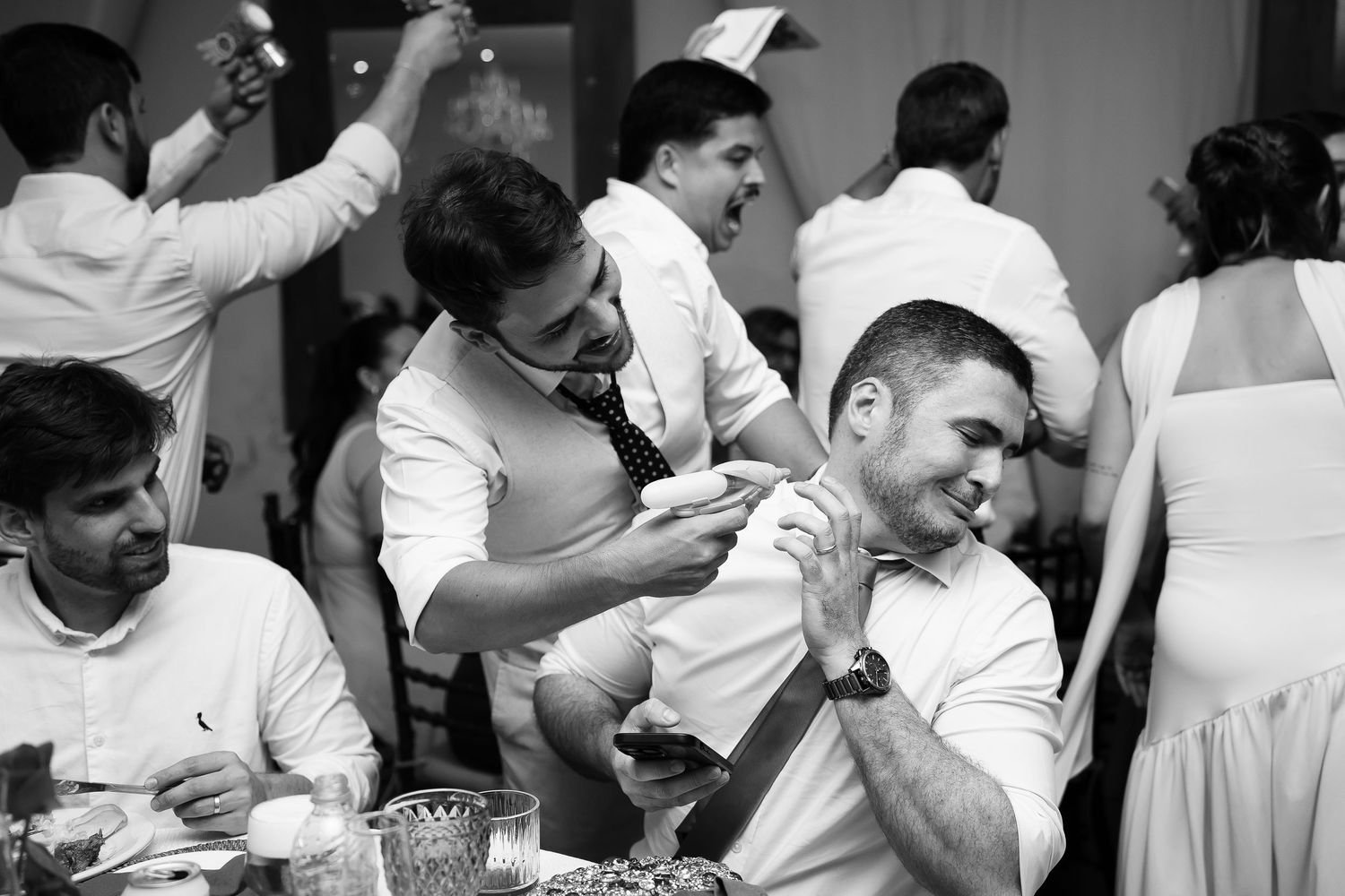 Black and white photo of guests laughing and interacting at a lively wedding reception dinner table.