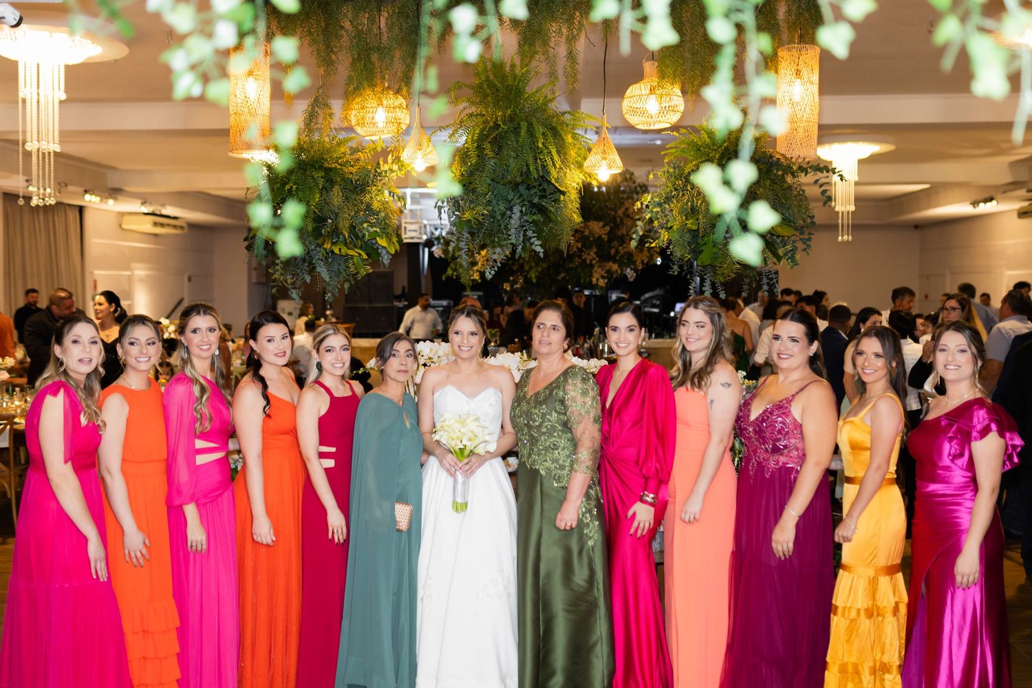 Bride in white gown poses with colorful bridesmaids in vibrant rainbow dresses at elegant wedding reception.