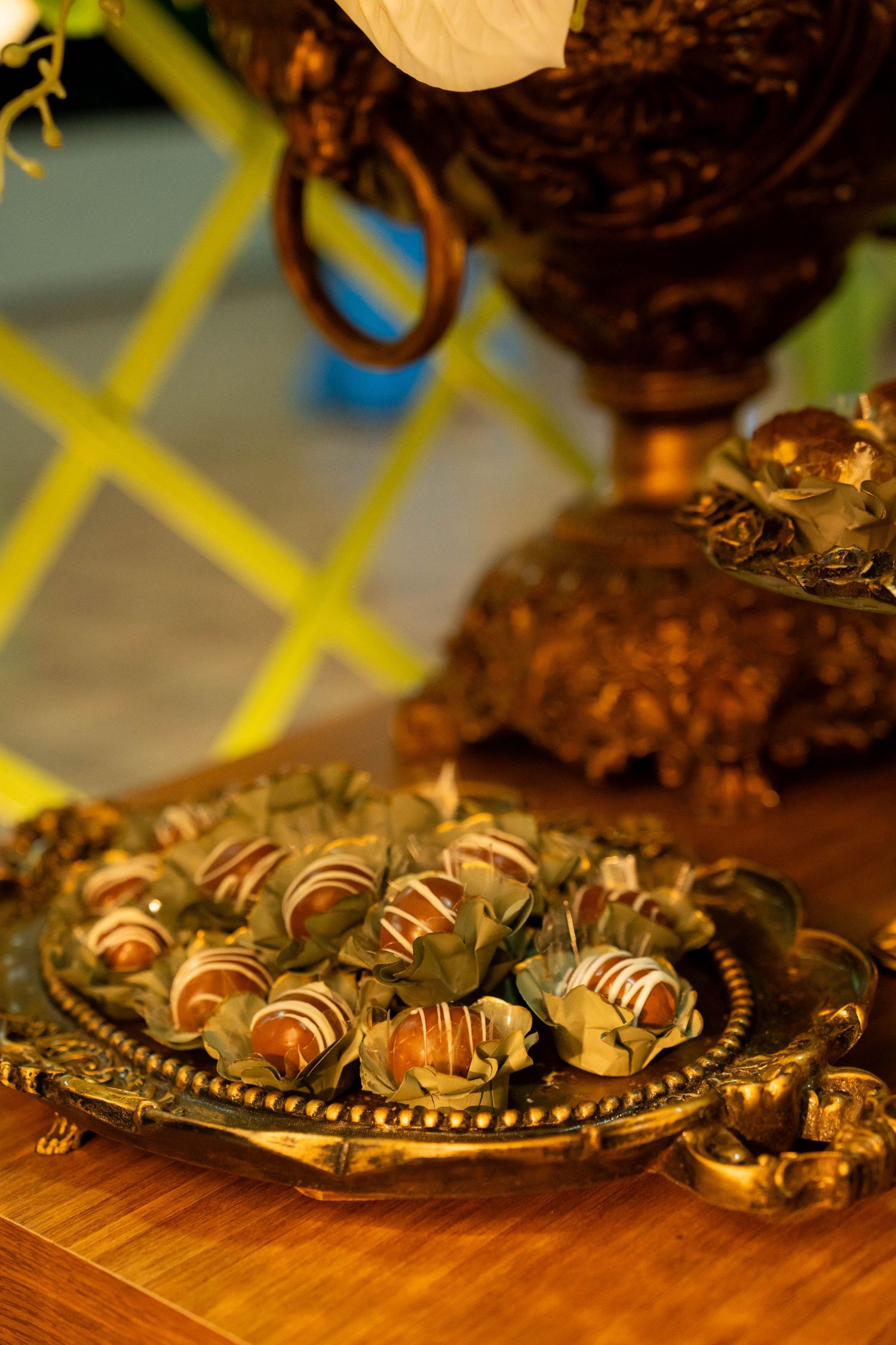 Ornate golden tray with chocolate truffles decorated with green leaves on a wooden table.