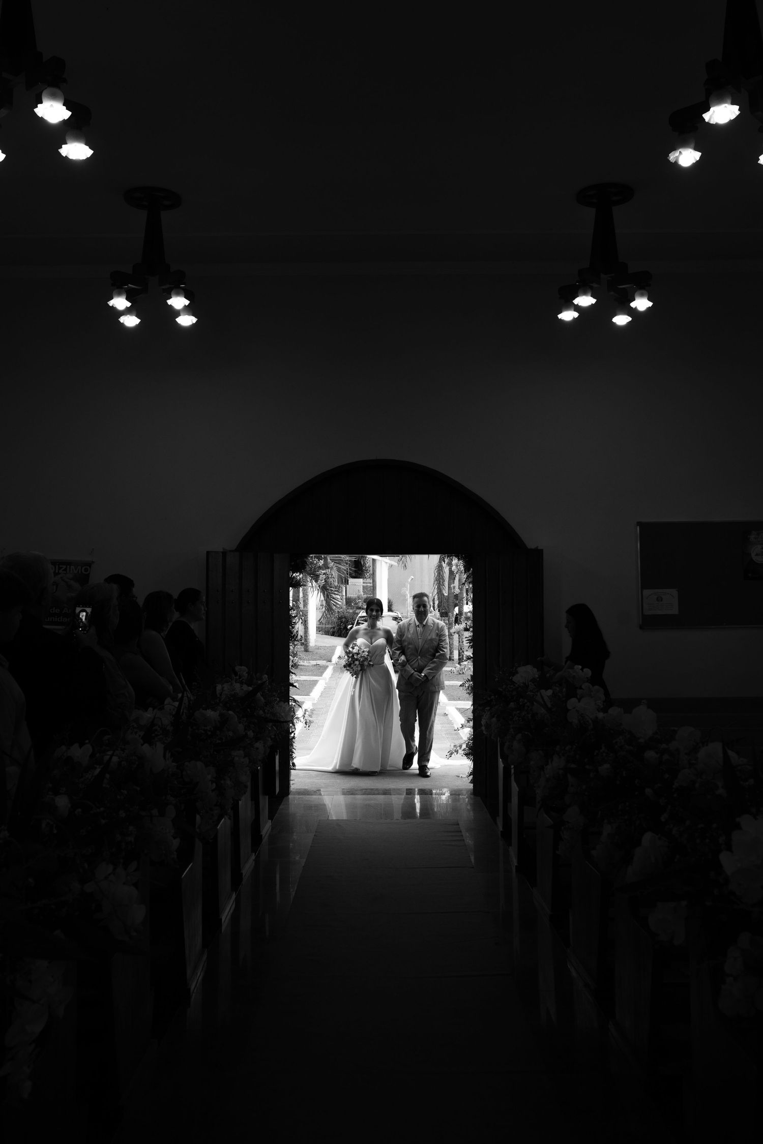 Black and white dramatic shot of a bride and escort framed in a church archway before walking the aisle.