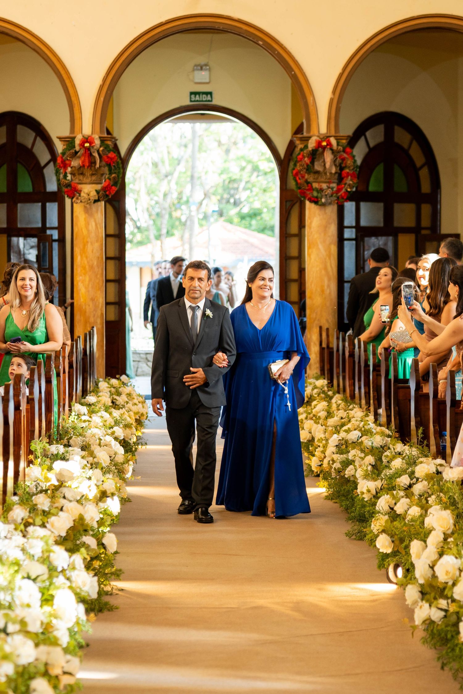 Couple walks down flower-lined church aisle at wedding ceremony, woman in blue gown, man in gray suit.