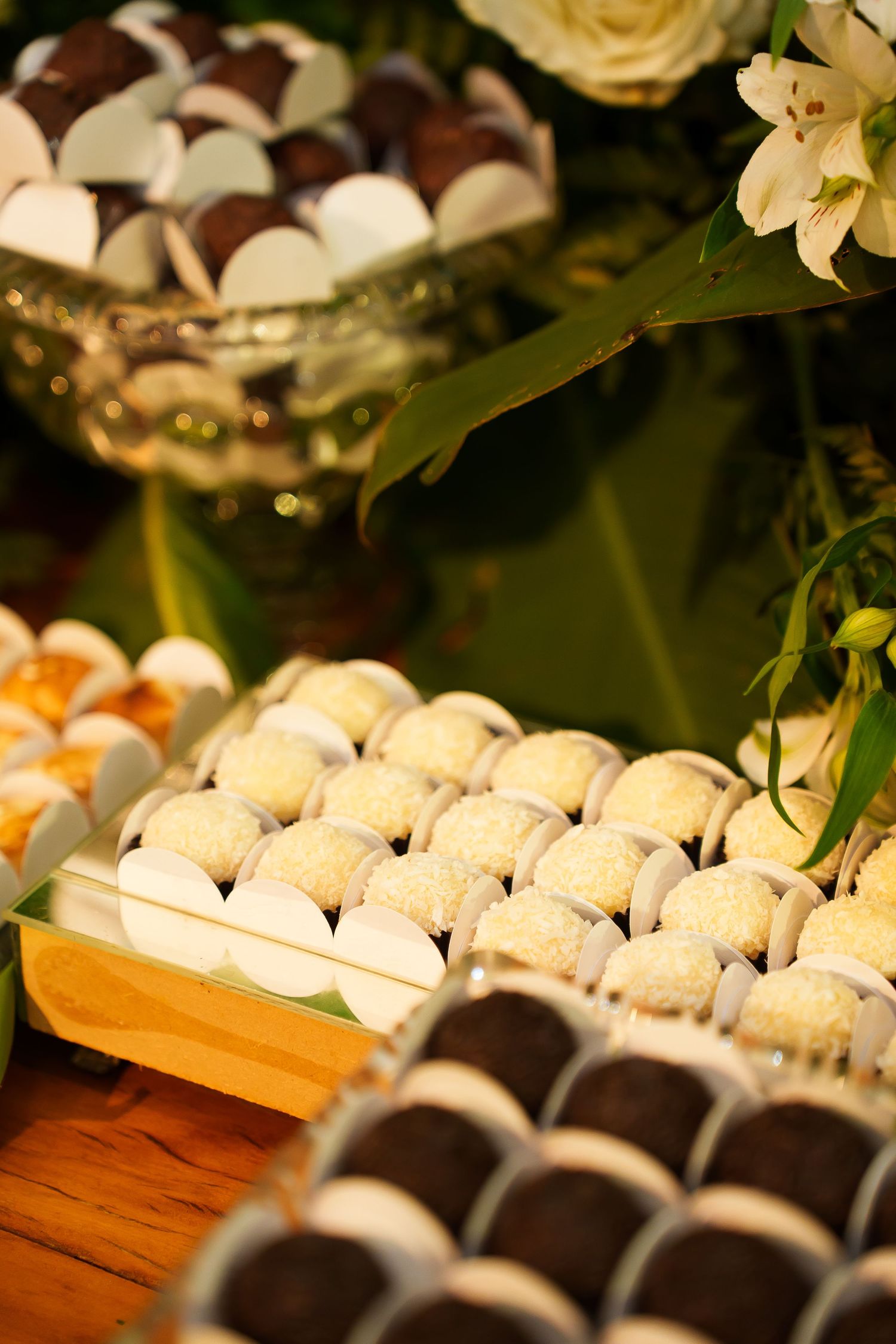 Elegant dessert table with coconut truffles, chocolate bonbons, and white flowers at a wedding reception.