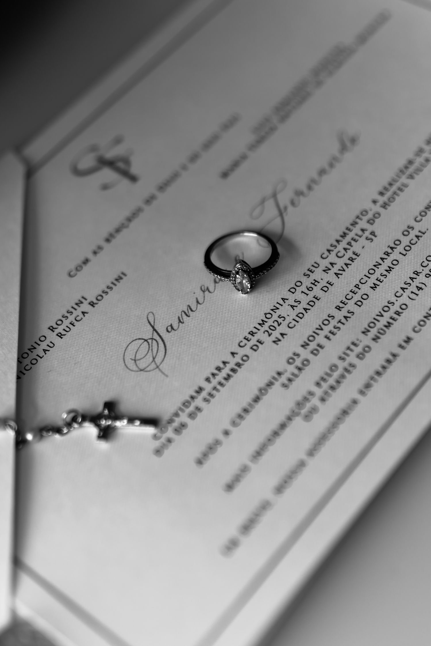 Black and white photo of a diamond engagement ring resting on elegant wedding invitation stationery.