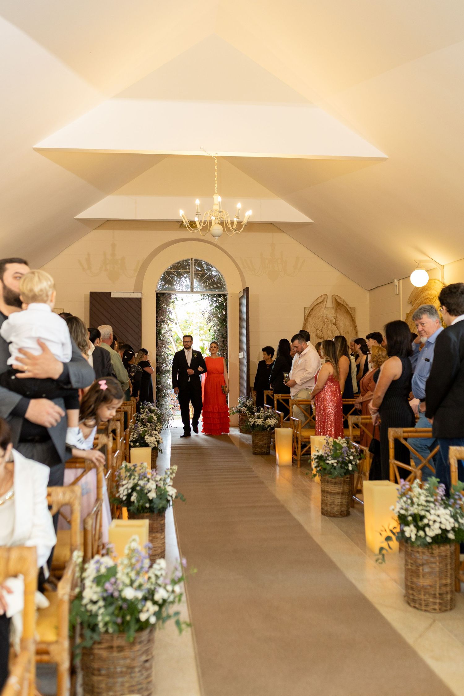 Elegant wedding ceremony aisle with floral arrangements in wicker baskets, guests standing, and couple walking toward altar.