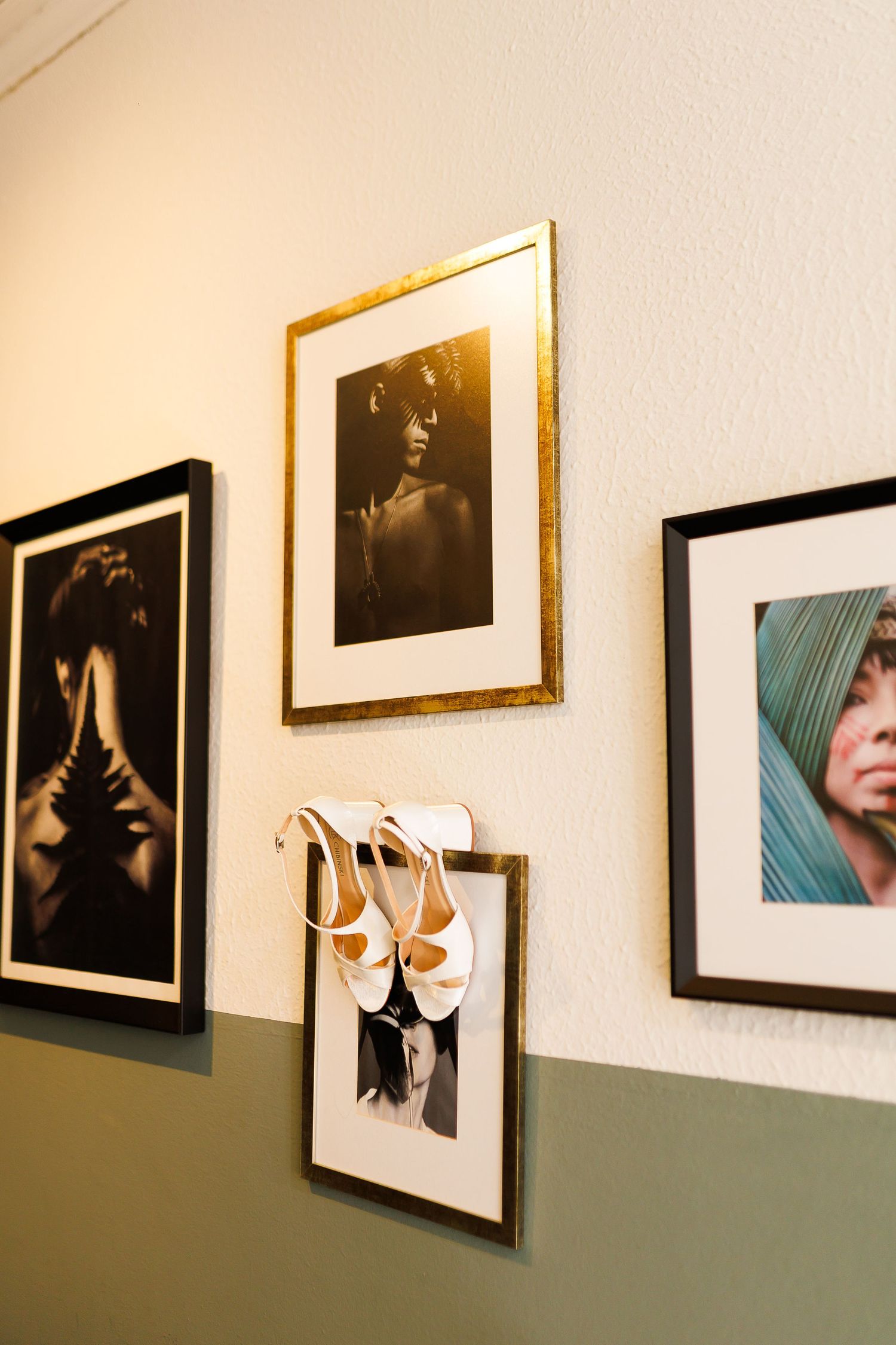 Gallery wall with framed black and white portraits and a colorful photo, with white heeled sandals hanging on a frame.