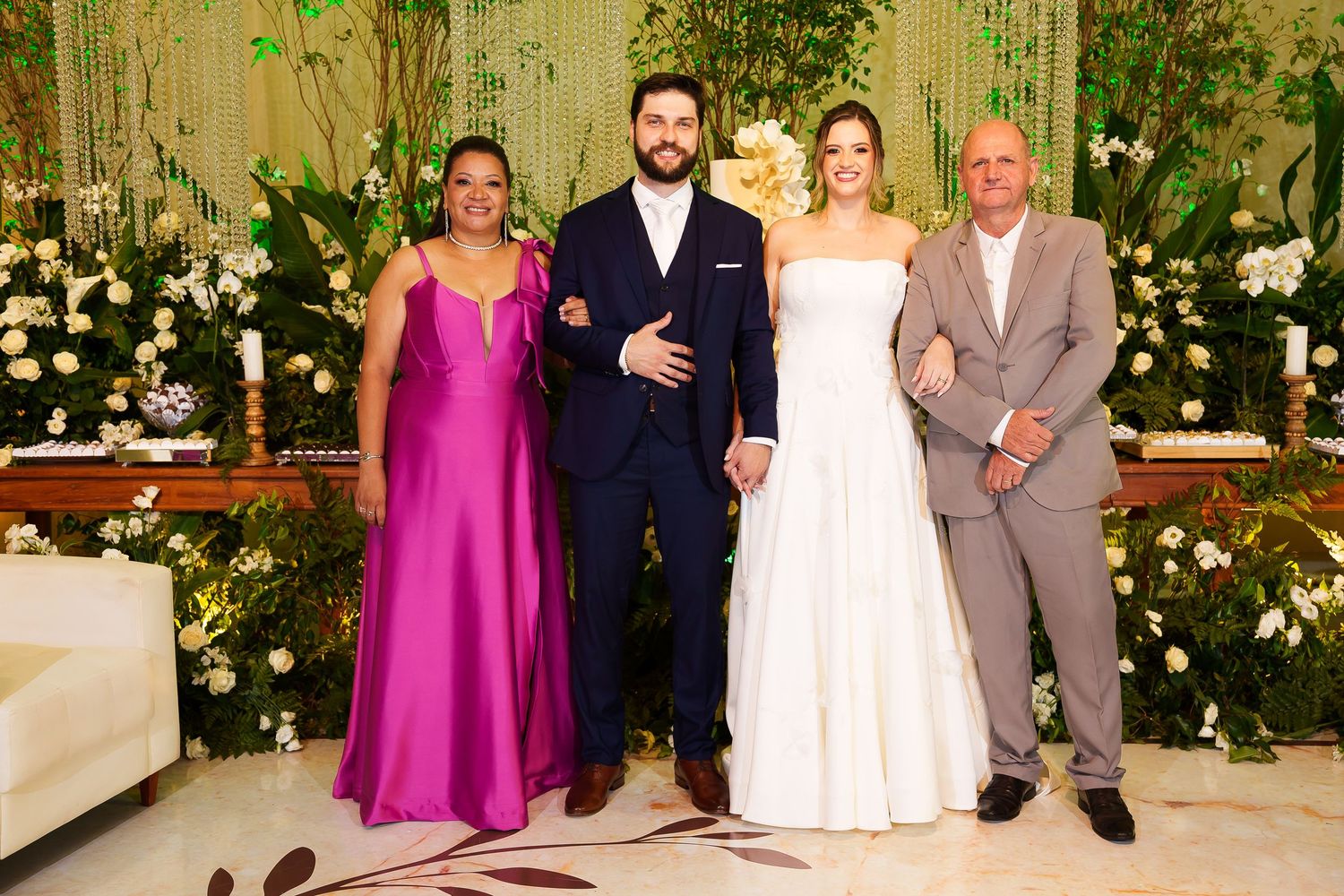 Wedding party of four posing elegantly, bride in white gown, groom in navy suit, guests in fuchsia dress and gray suit.