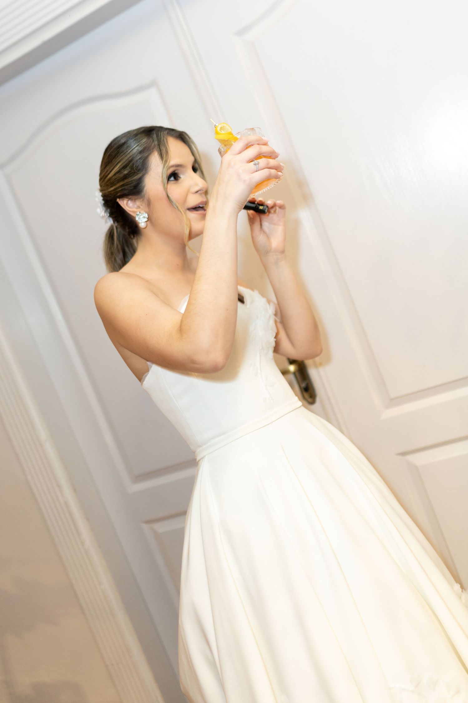 Bride in white strapless ball gown holding a yellow rubber duck up near a door at her wedding reception.