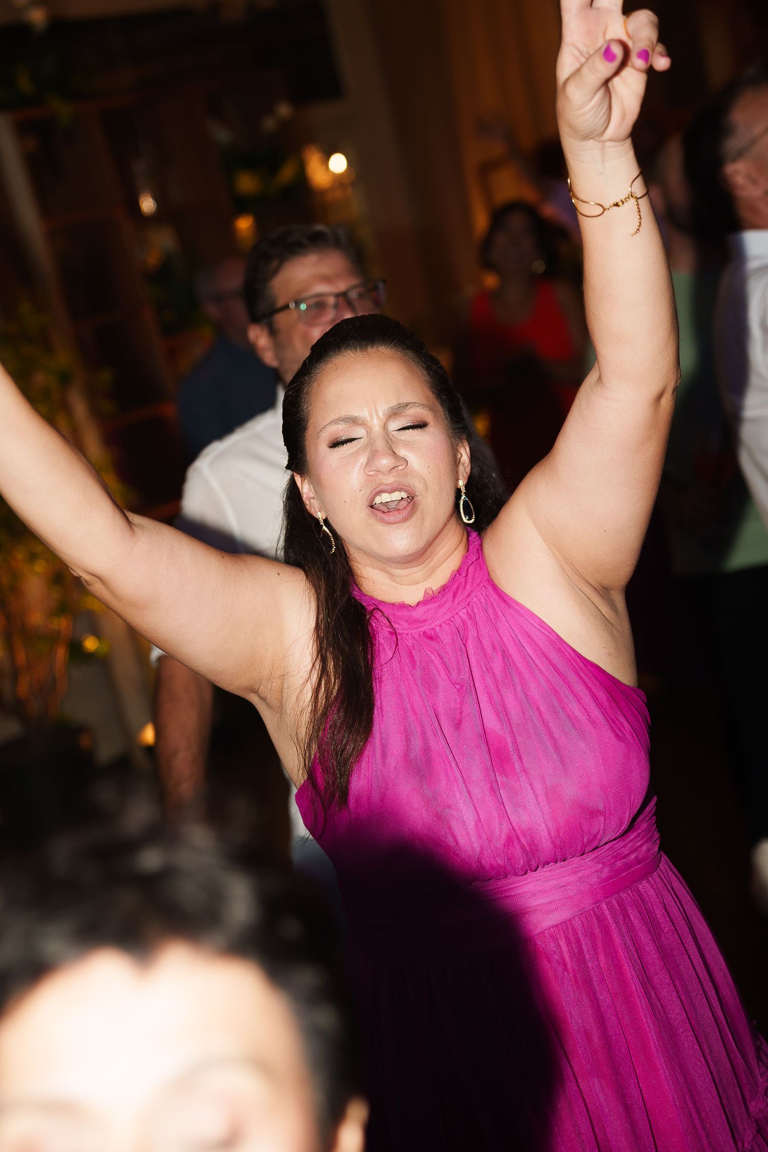 Woman in pink dress dancing joyfully with arms raised at a party or wedding celebration.
