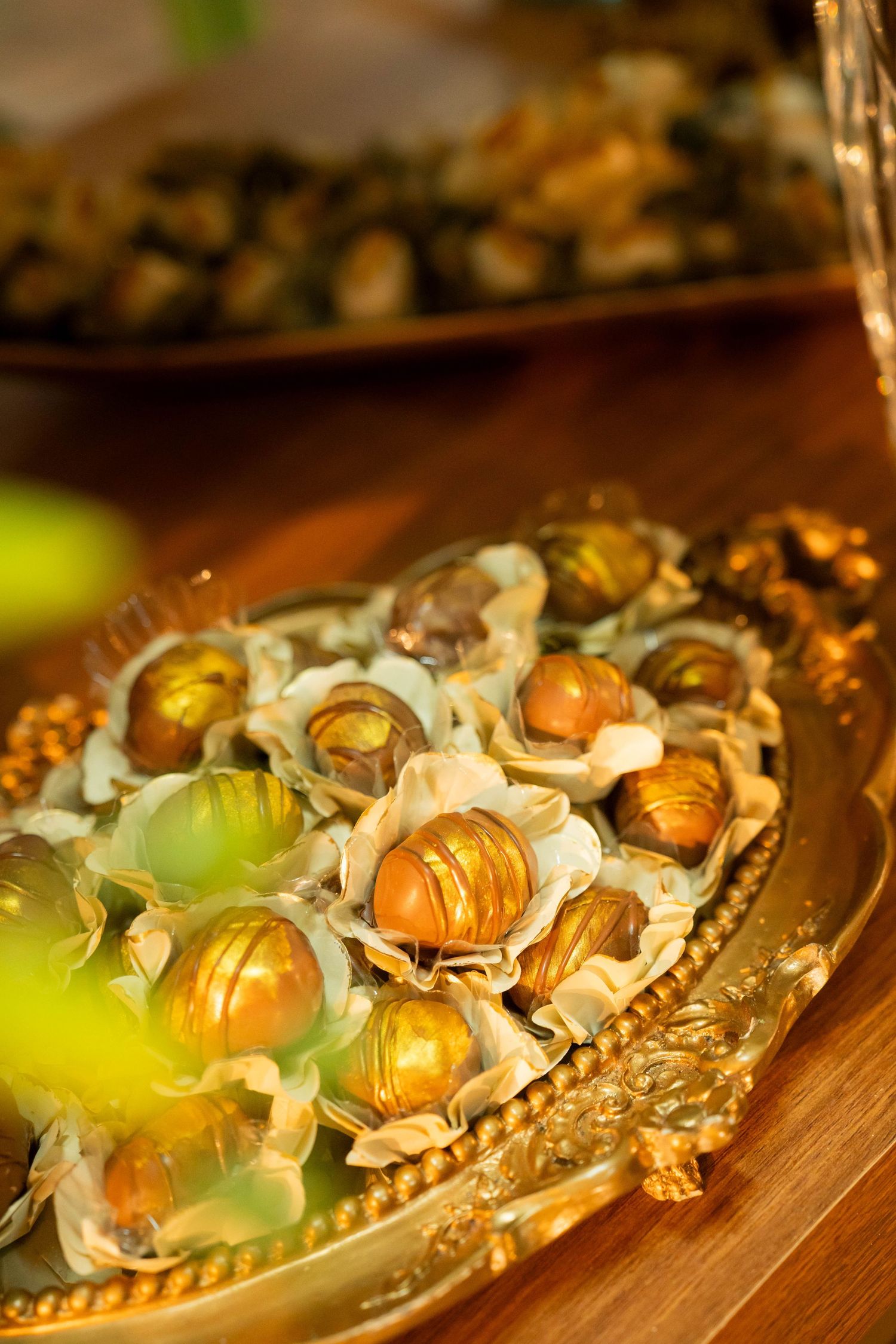 Elegant gold chocolate truffles in decorative white paper cups arranged on an ornate golden tray.