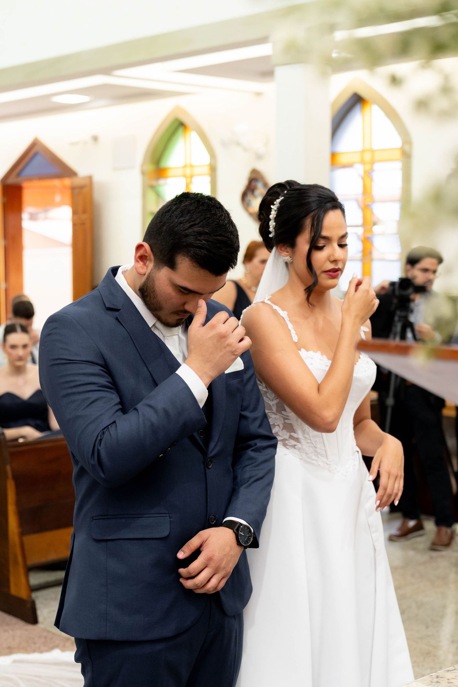 Bride and groom praying together during wedding ceremony in a church with colorful stained glass windows.