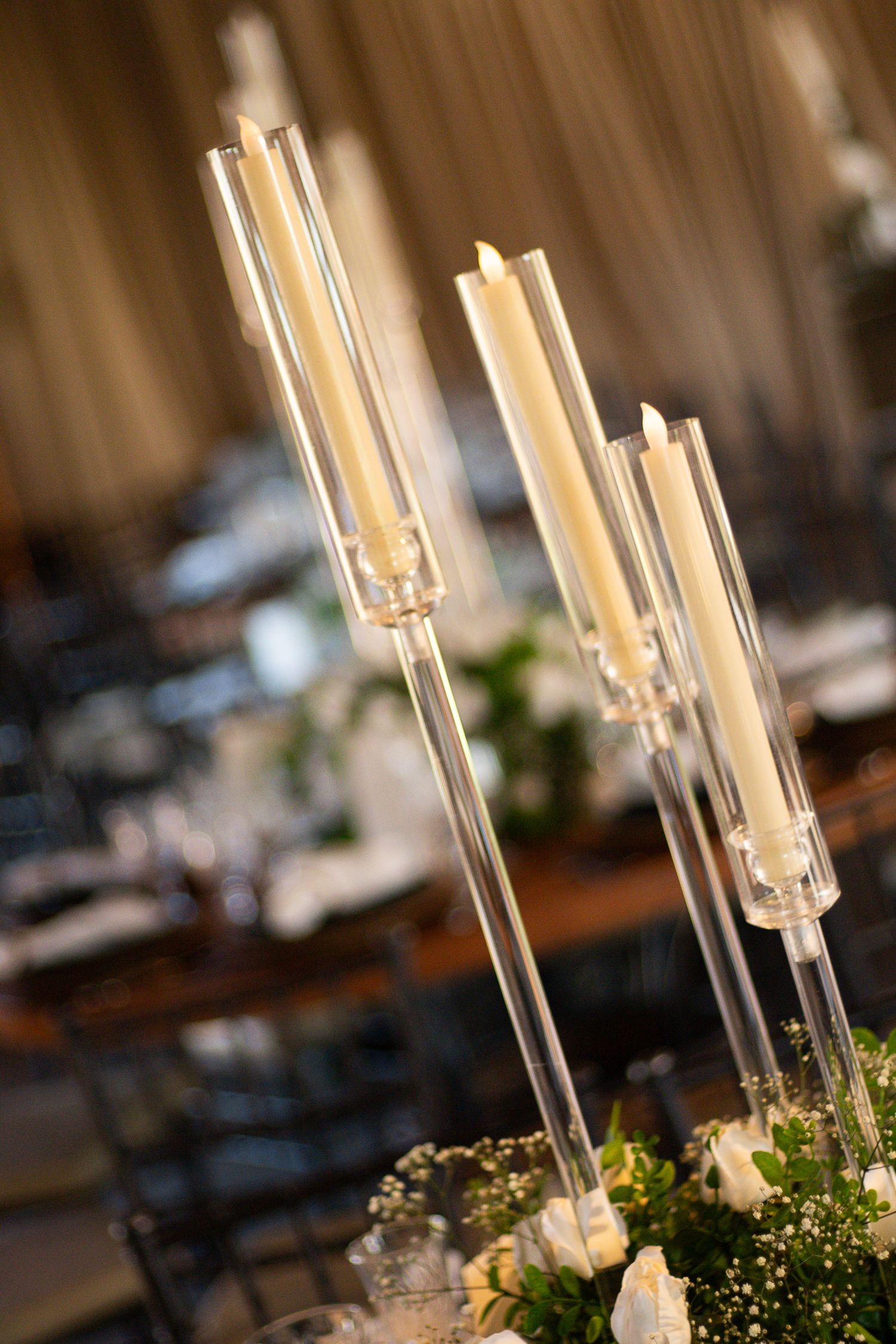 Elegant glass candelabras with tall white taper candles on a floral centerpiece at a formal wedding reception.