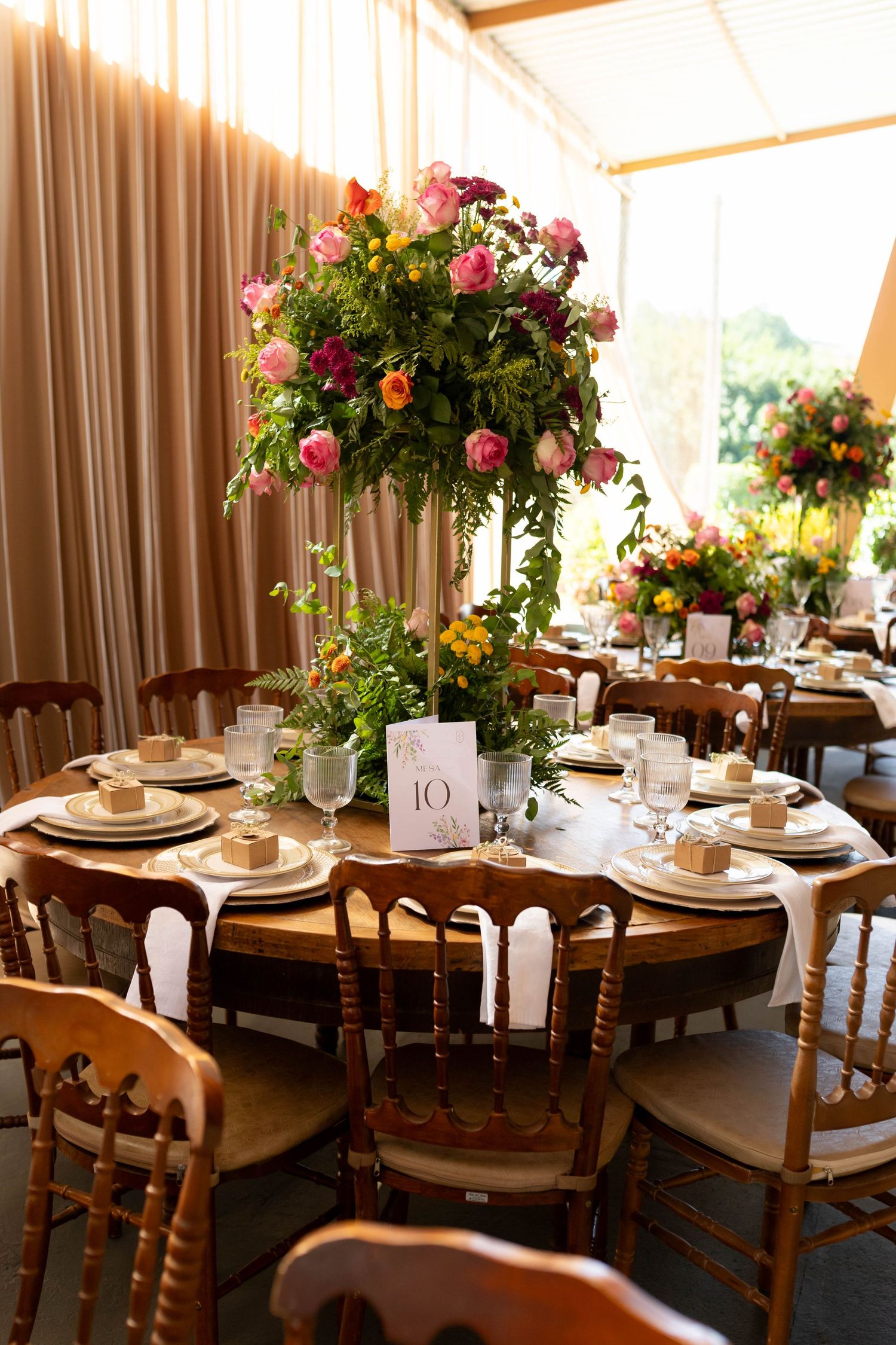 Elegant wedding reception table with tall floral centerpiece of pink roses, round wood table, place settings, and table number 10.