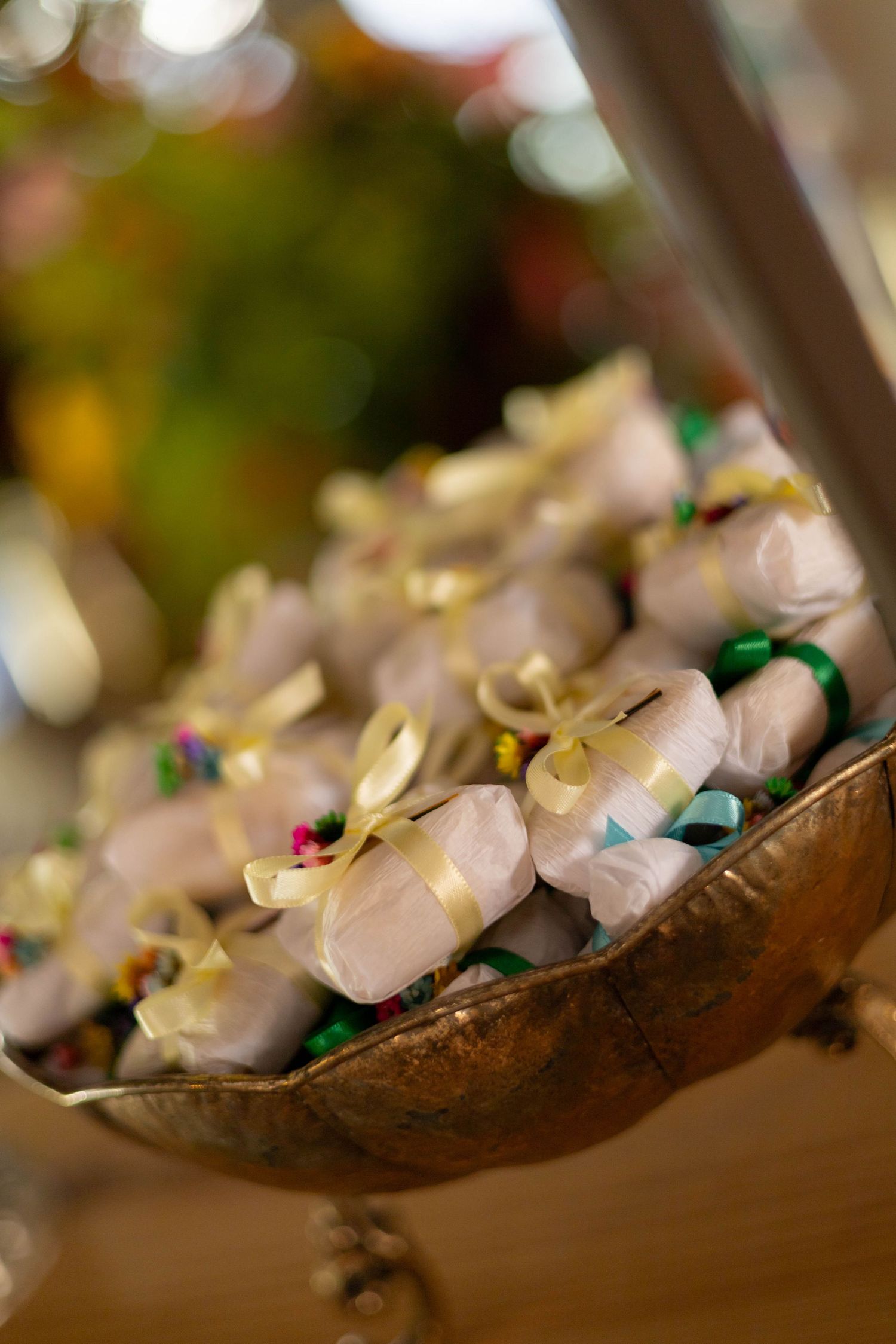 Gold-ribbon wrapped candy favors displayed in an ornate bronze bowl at a festive celebration.