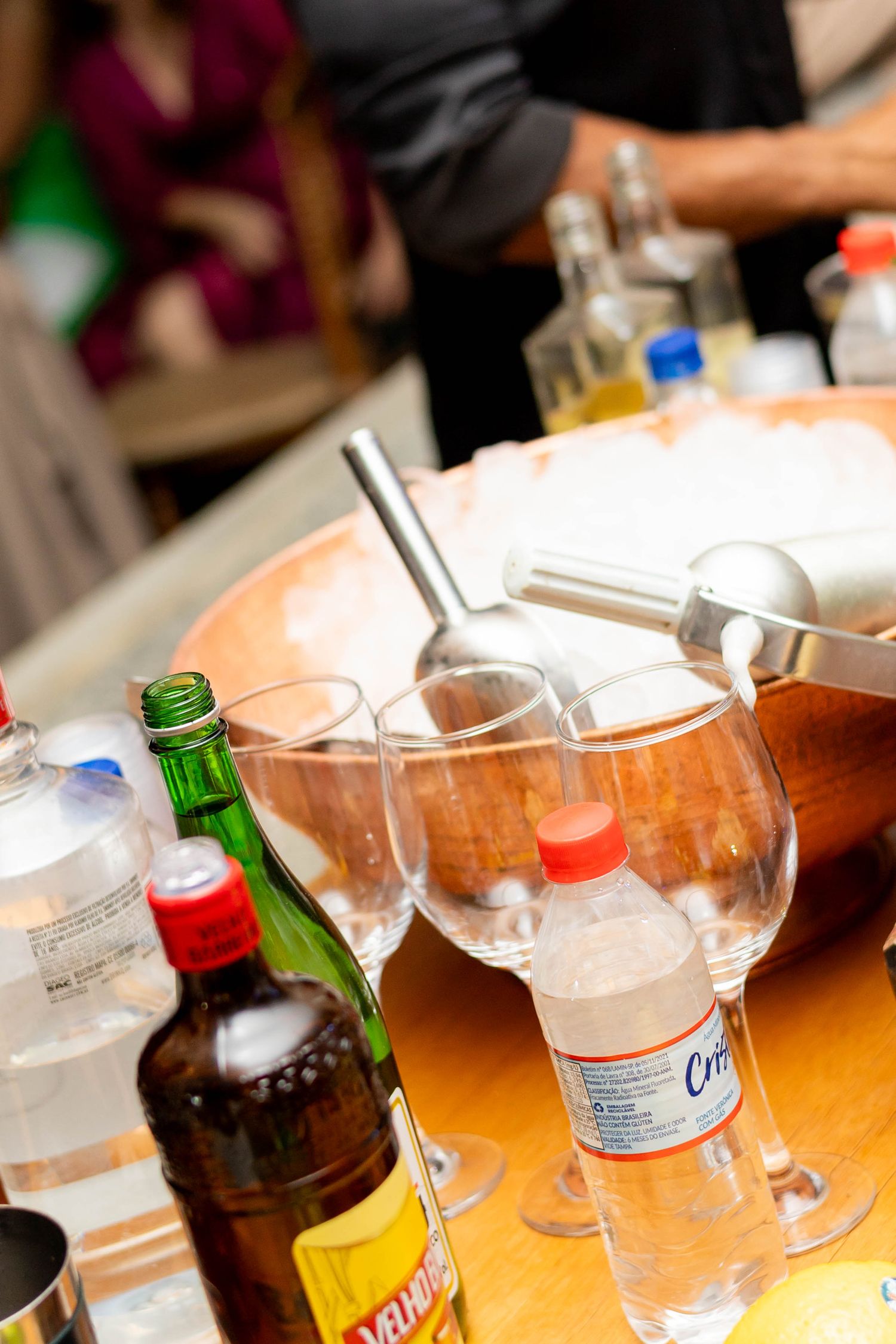 Assorted liquor bottles and wine glasses on a bar table with an ice bucket at a party event.