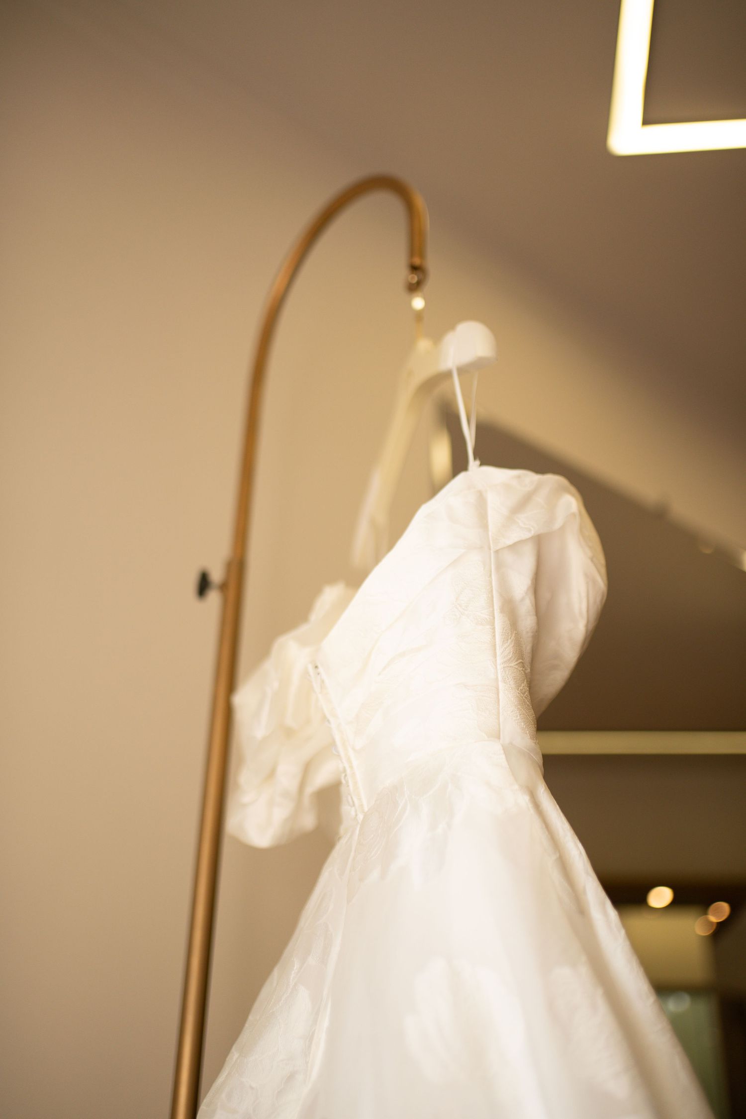White wedding dress with puffed sleeves hanging on a gold rack in a bridal boutique.
