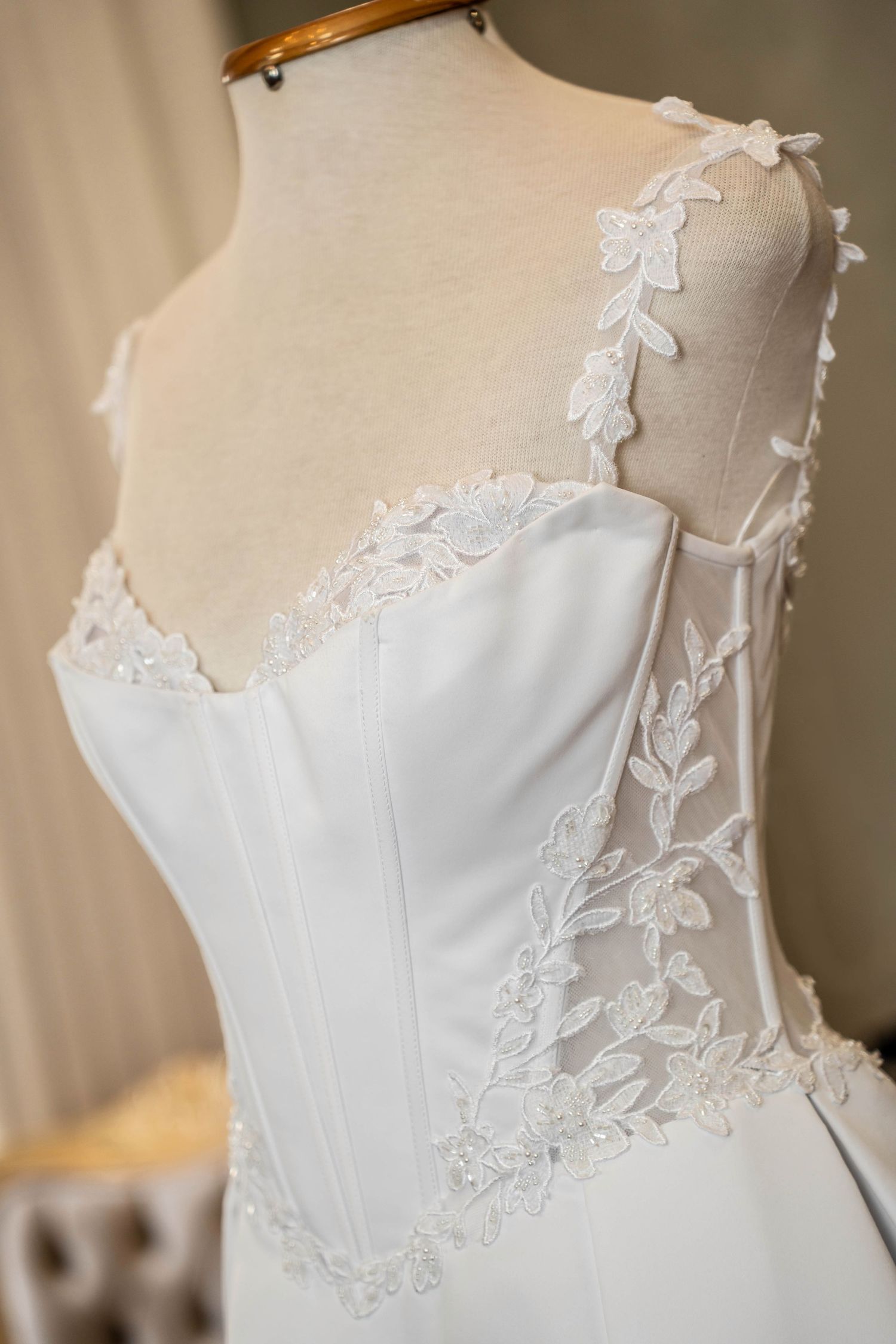 Elegant white wedding dress on mannequin featuring delicate lace applique details and corset bodice design.