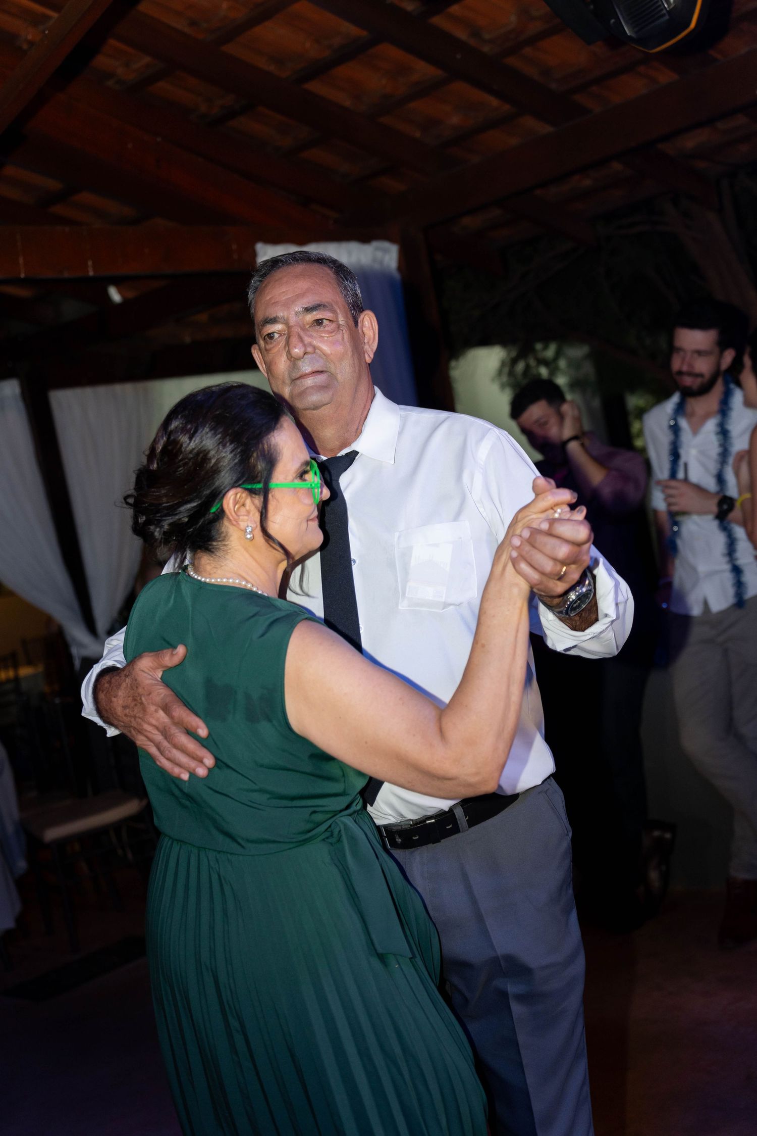 Couple sharing a romantic dance at a wedding reception, woman in green dress, man in white shirt and tie.