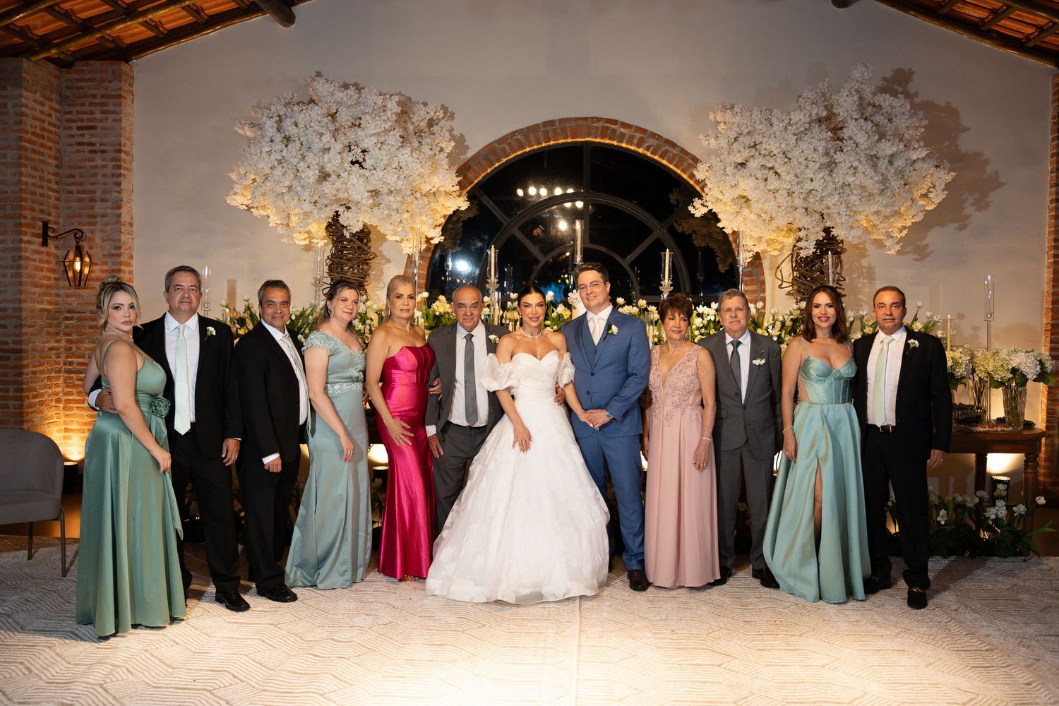 Wedding party poses elegantly in a decorated venue with floral arches, bride in white gown, bridesmaids in sage and pink.