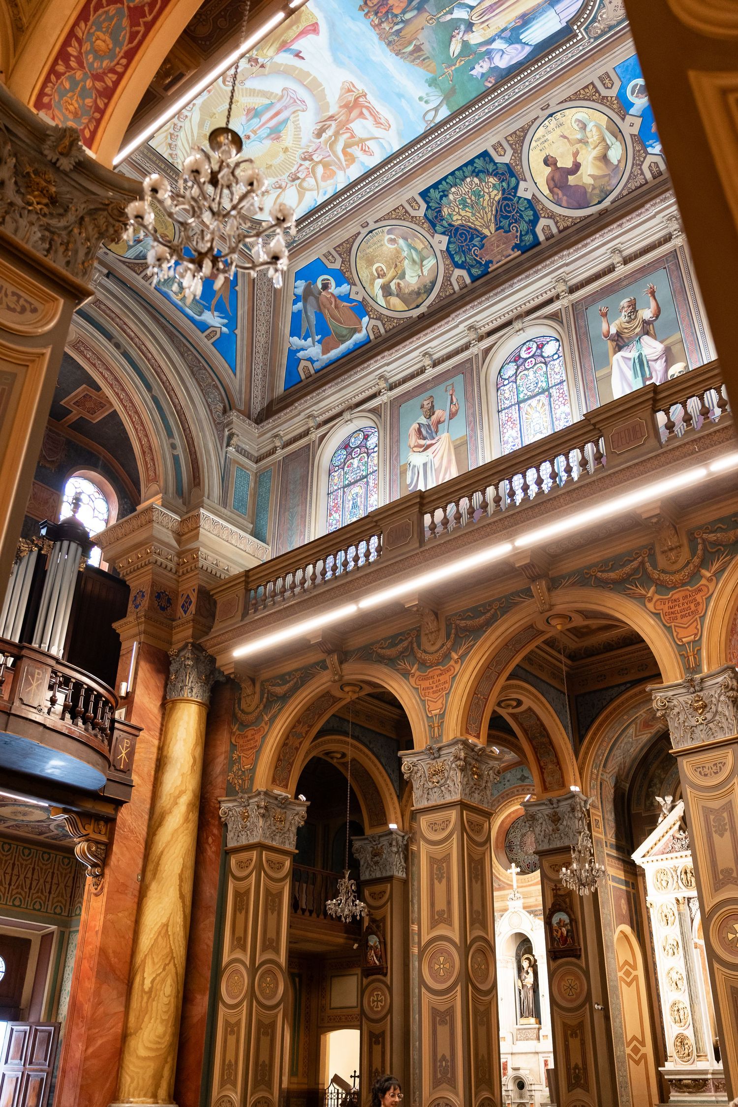 Ornate church interior with colorful frescoes, arched columns, chandelier, and detailed ceiling paintings in baroque style.