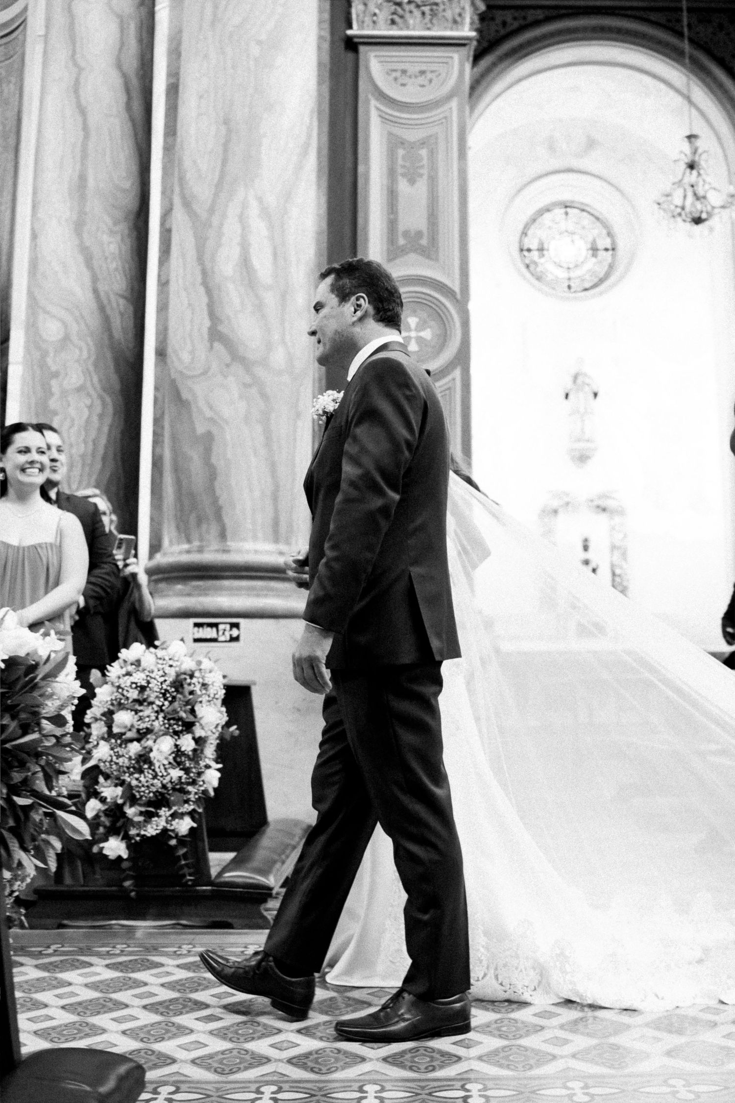 Black and white photo of groom walking toward bride in elegant church wedding ceremony.