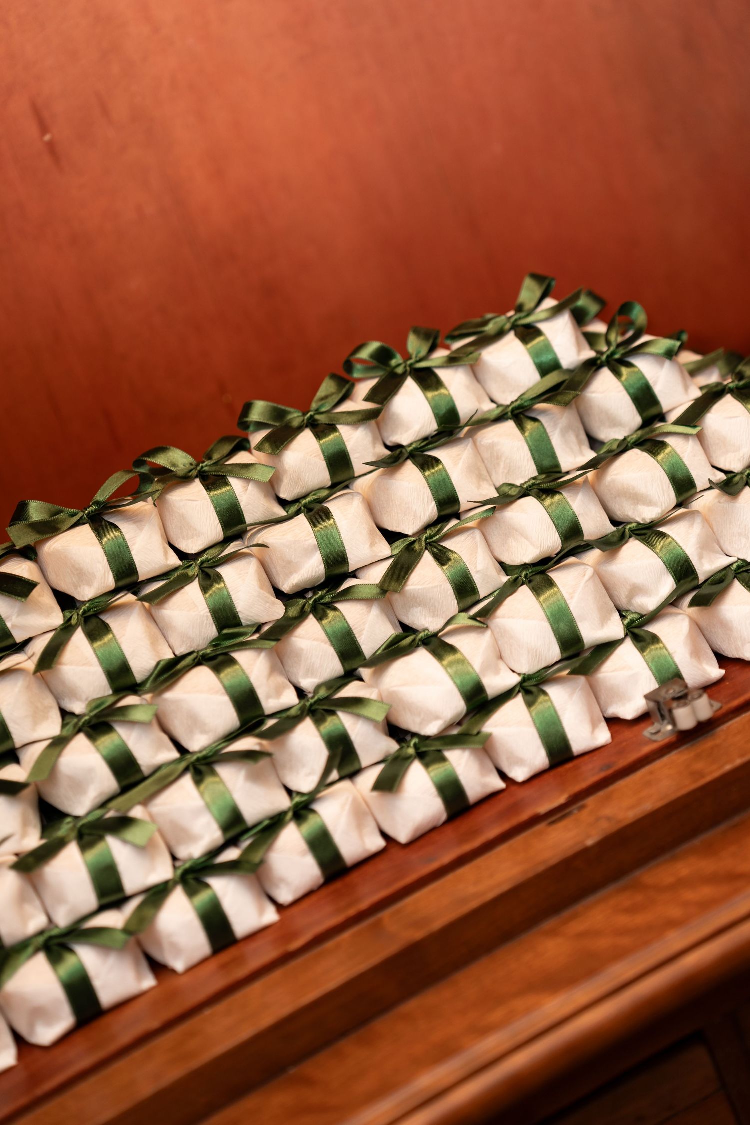 Rows of white gift favors tied with green satin ribbons displayed neatly on a wooden shelf.
