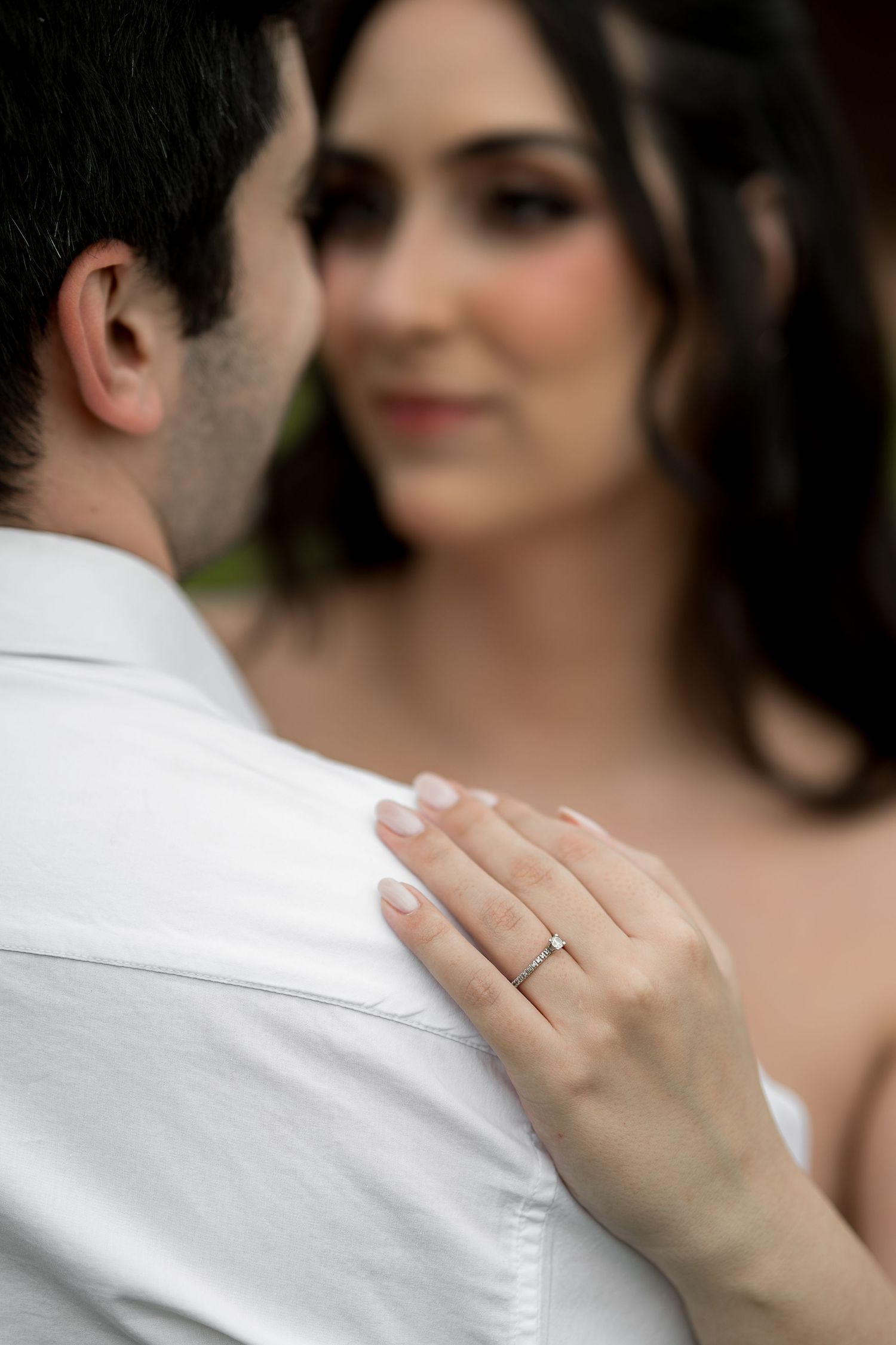 Close-up of a bride's hand with a diamond engagement ring resting on her groom's white dress shirt.