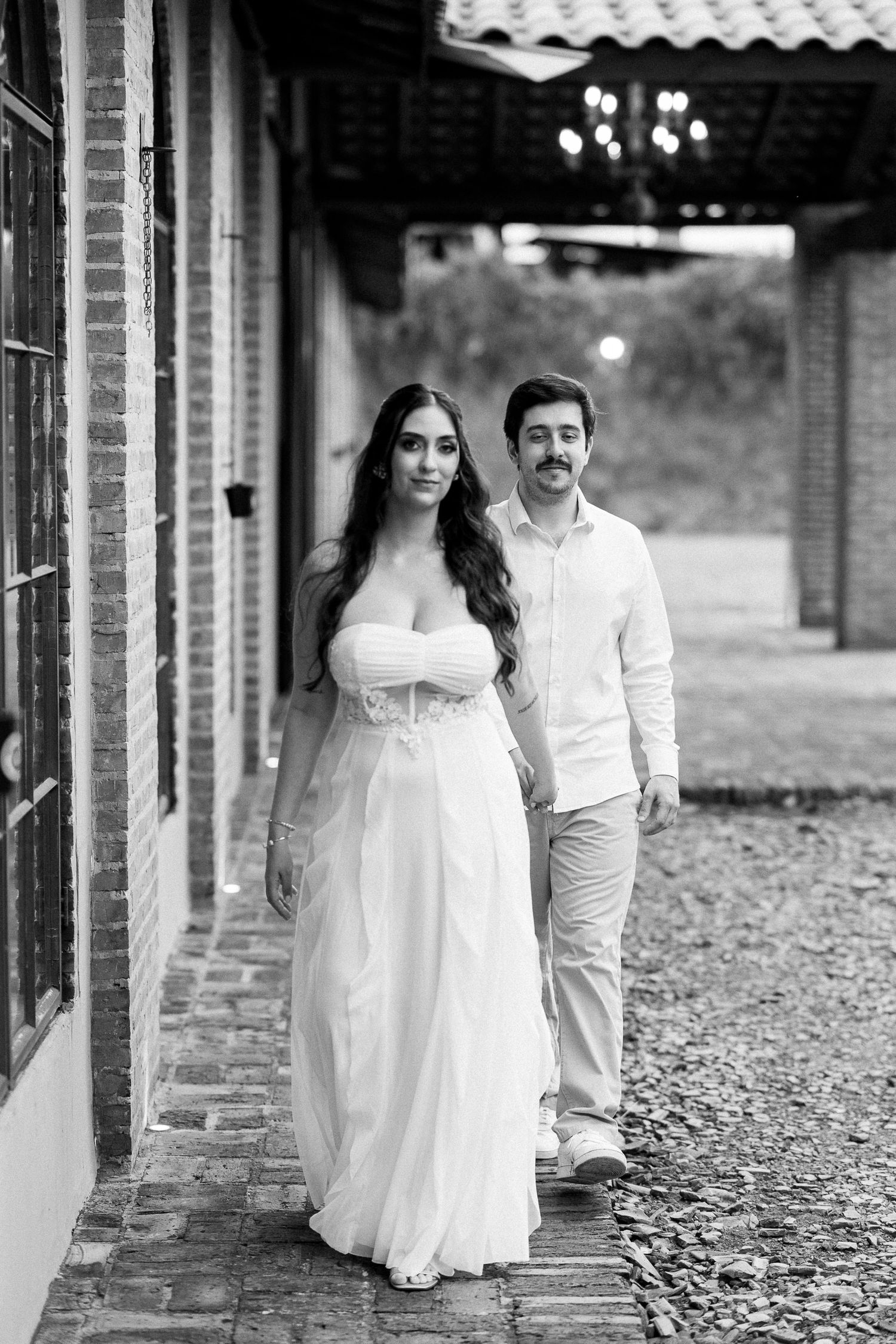 Black and white photo of bride and groom walking hand in hand along a brick building exterior.
