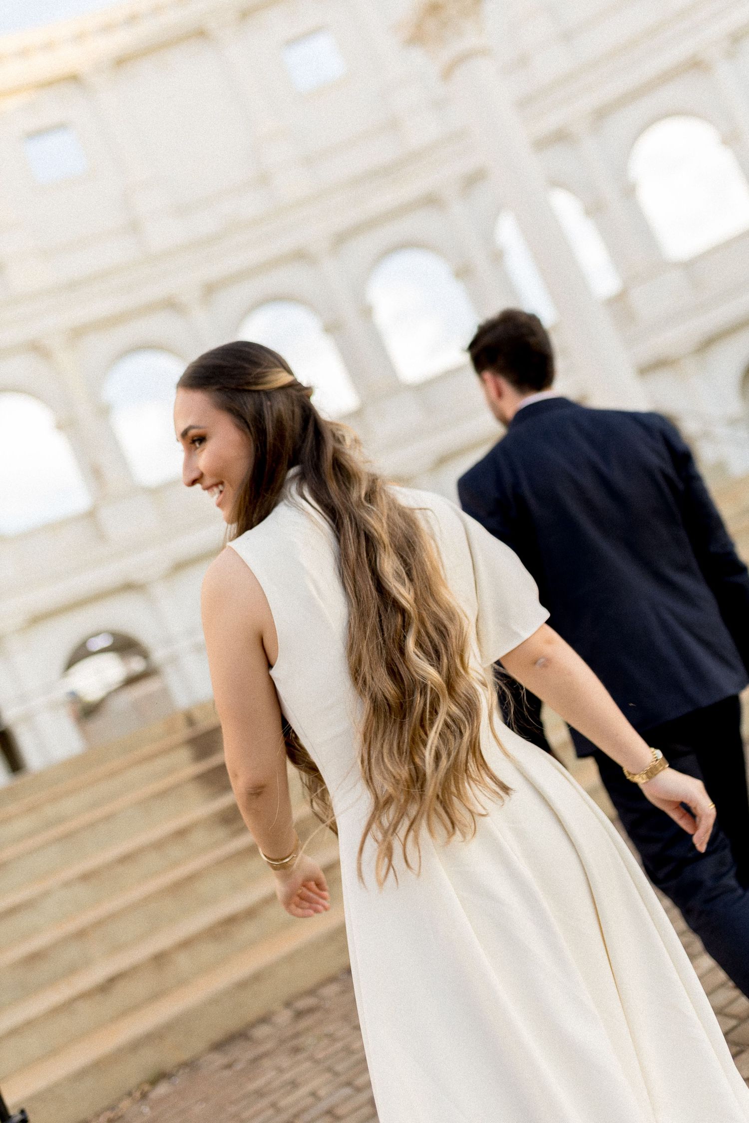 Bride in white dress smiles walking toward the Colosseum in Rome with groom in navy suit.