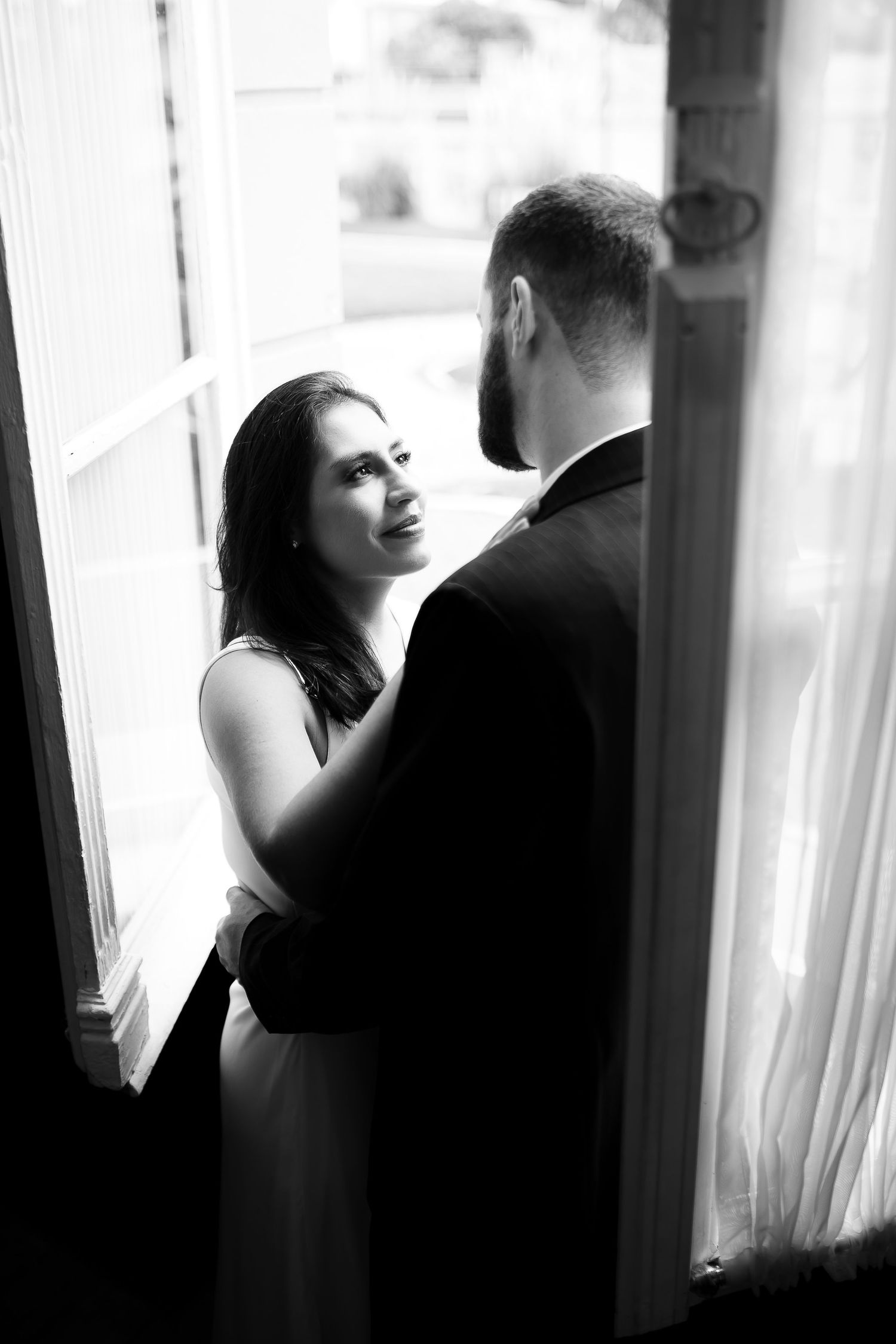 Black and white wedding photo of bride gazing up at groom while embracing in a doorway.