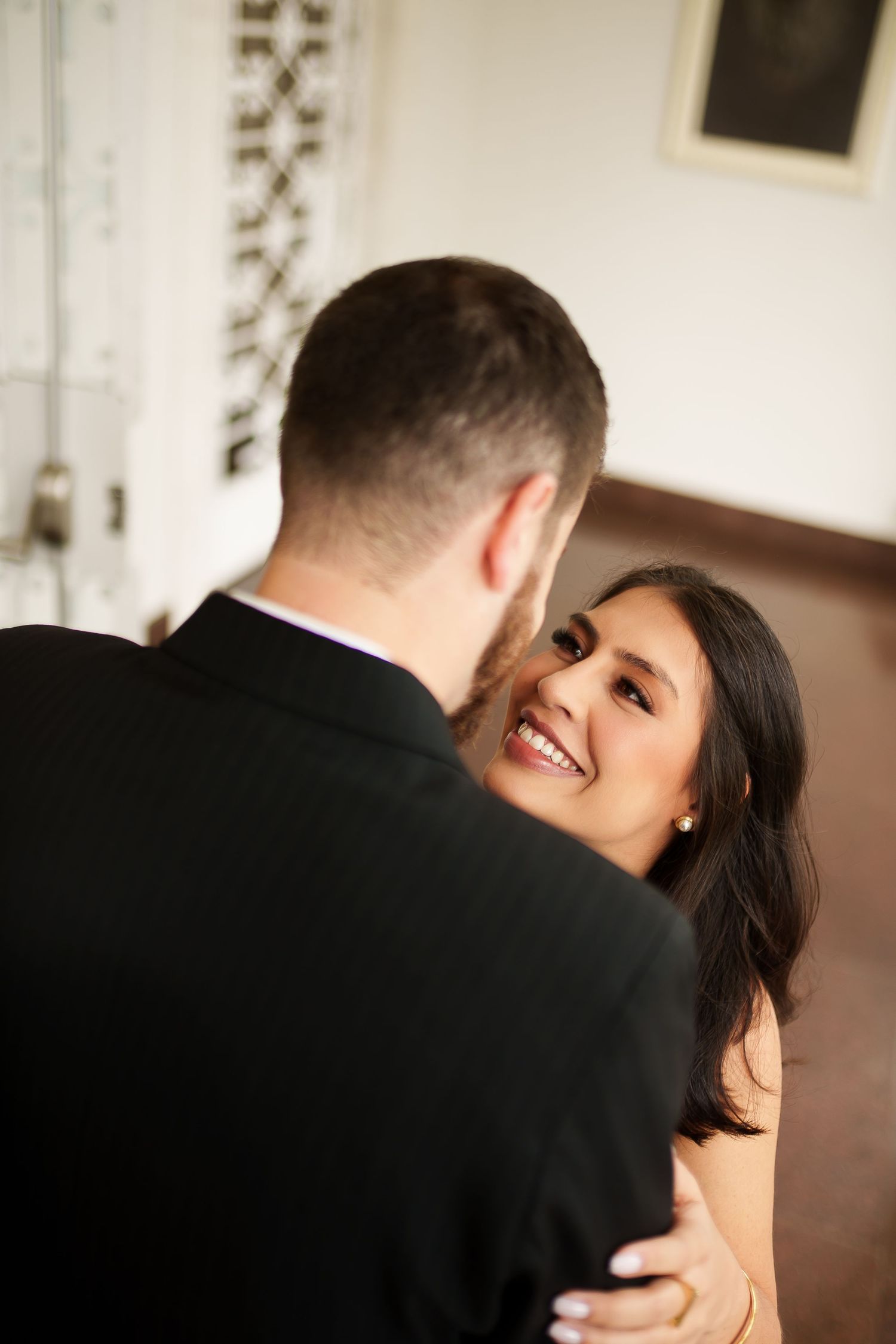 A smiling bride gazes lovingly at her groom during their first dance at an elegant indoor wedding venue.