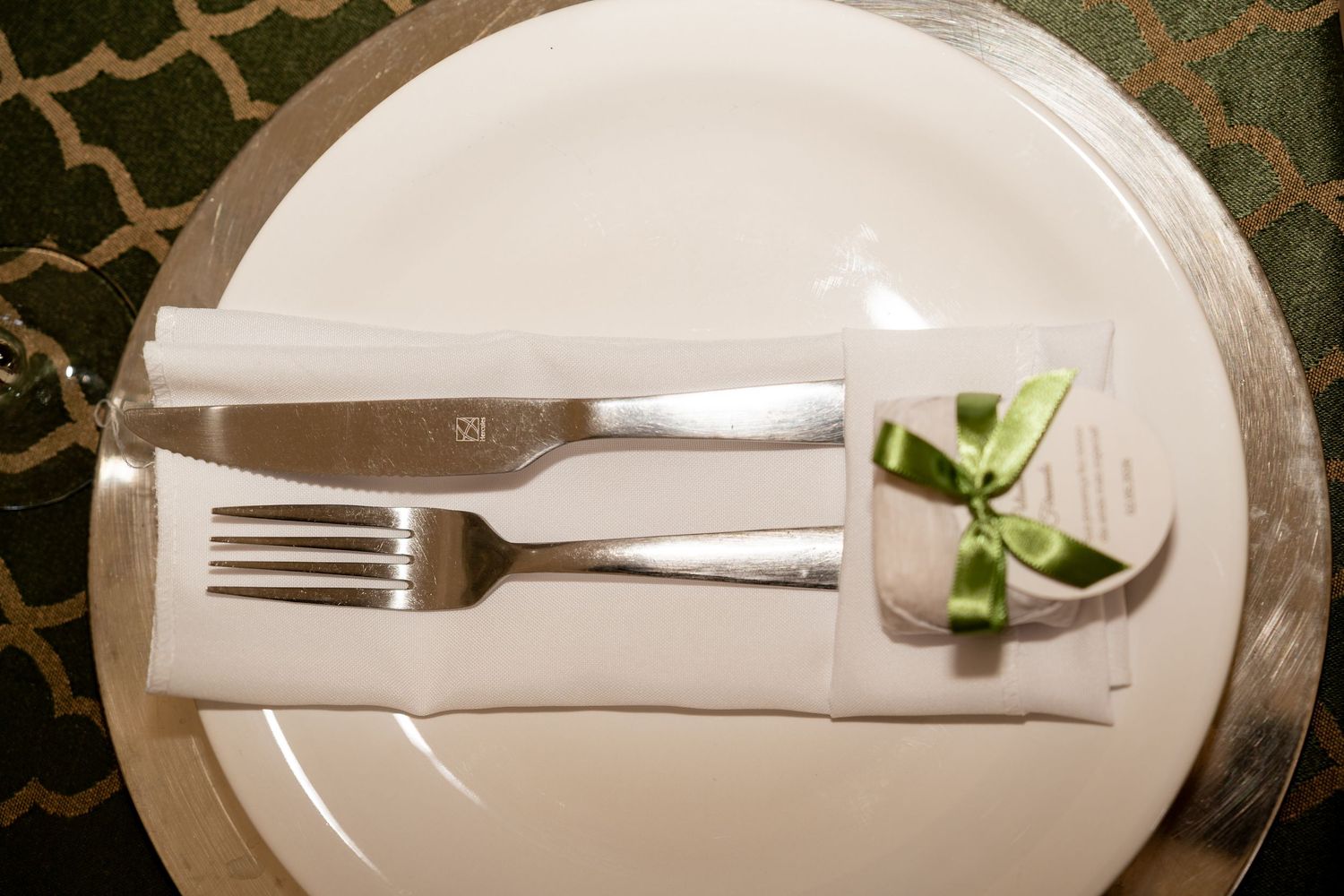 Elegant place setting with silver fork and knife on white plate, napkin tied with green ribbon bow.