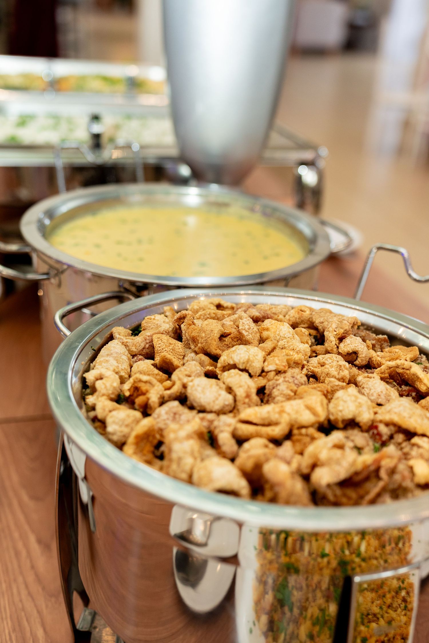 Buffet chafing dishes filled with crispy fried snacks and creamy yellow curry sauce at a catered event.