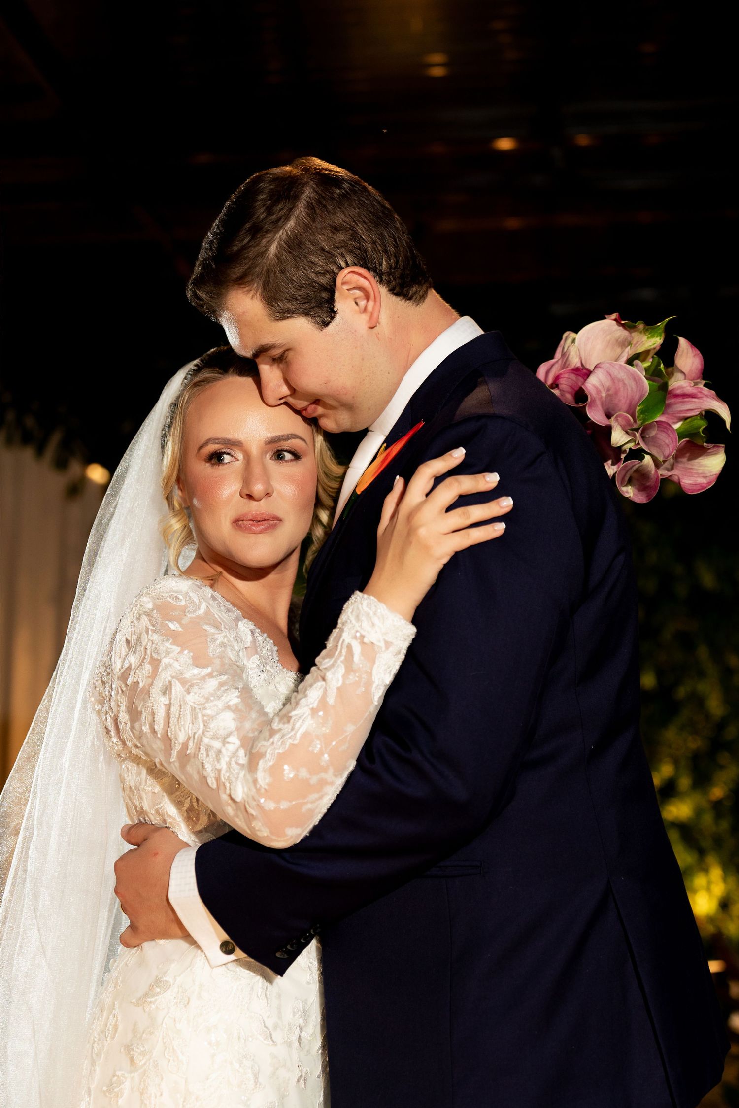 A bride and groom share an intimate first dance embrace, she in lace gown with veil, he in navy suit with orange tie.
