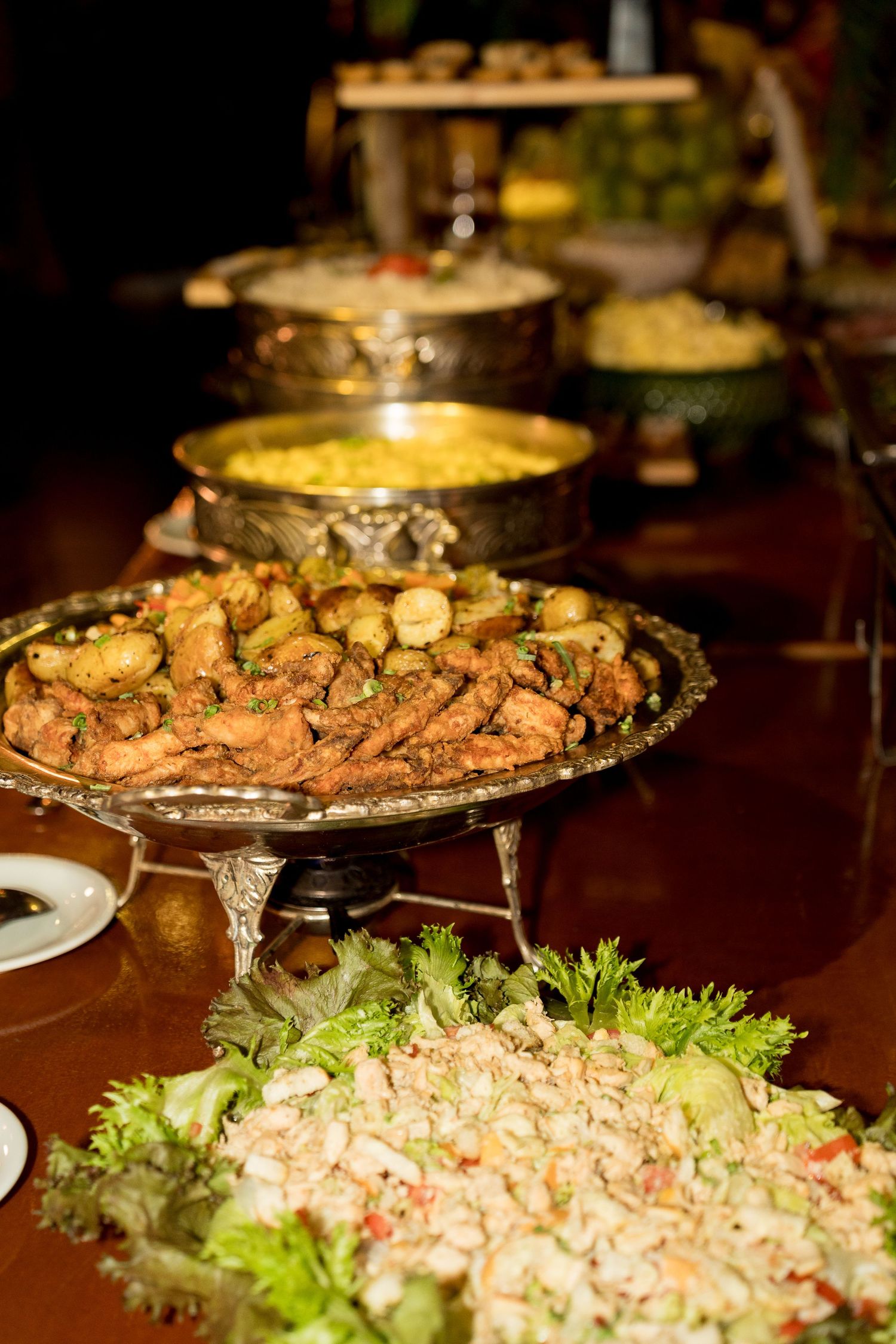 Elegant buffet spread featuring fried appetizers, curry dishes, and fresh salads displayed on ornate silver serving platters.