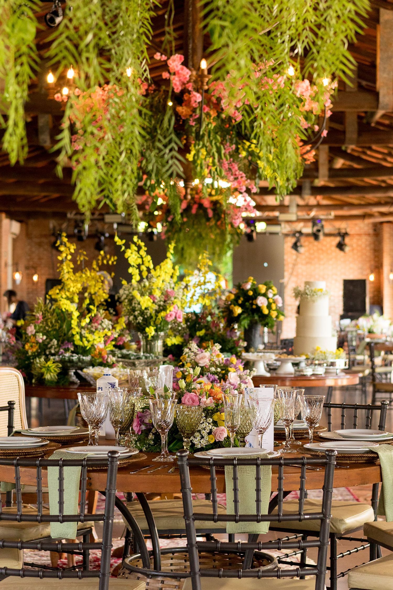 Elegant wedding reception with hanging greenery, pink flowers, crystal glasses, and floral centerpieces on rustic wooden tables.