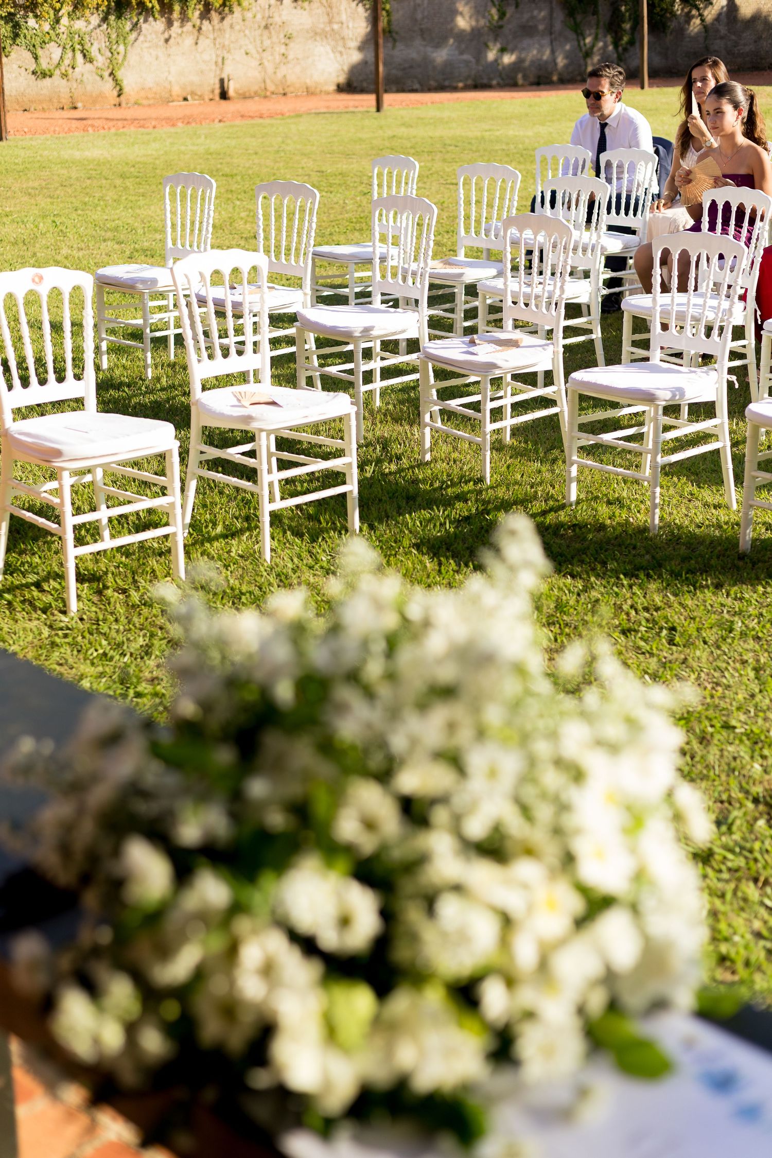 White chairs arranged on green grass for an outdoor wedding ceremony with floral arrangements in the foreground.