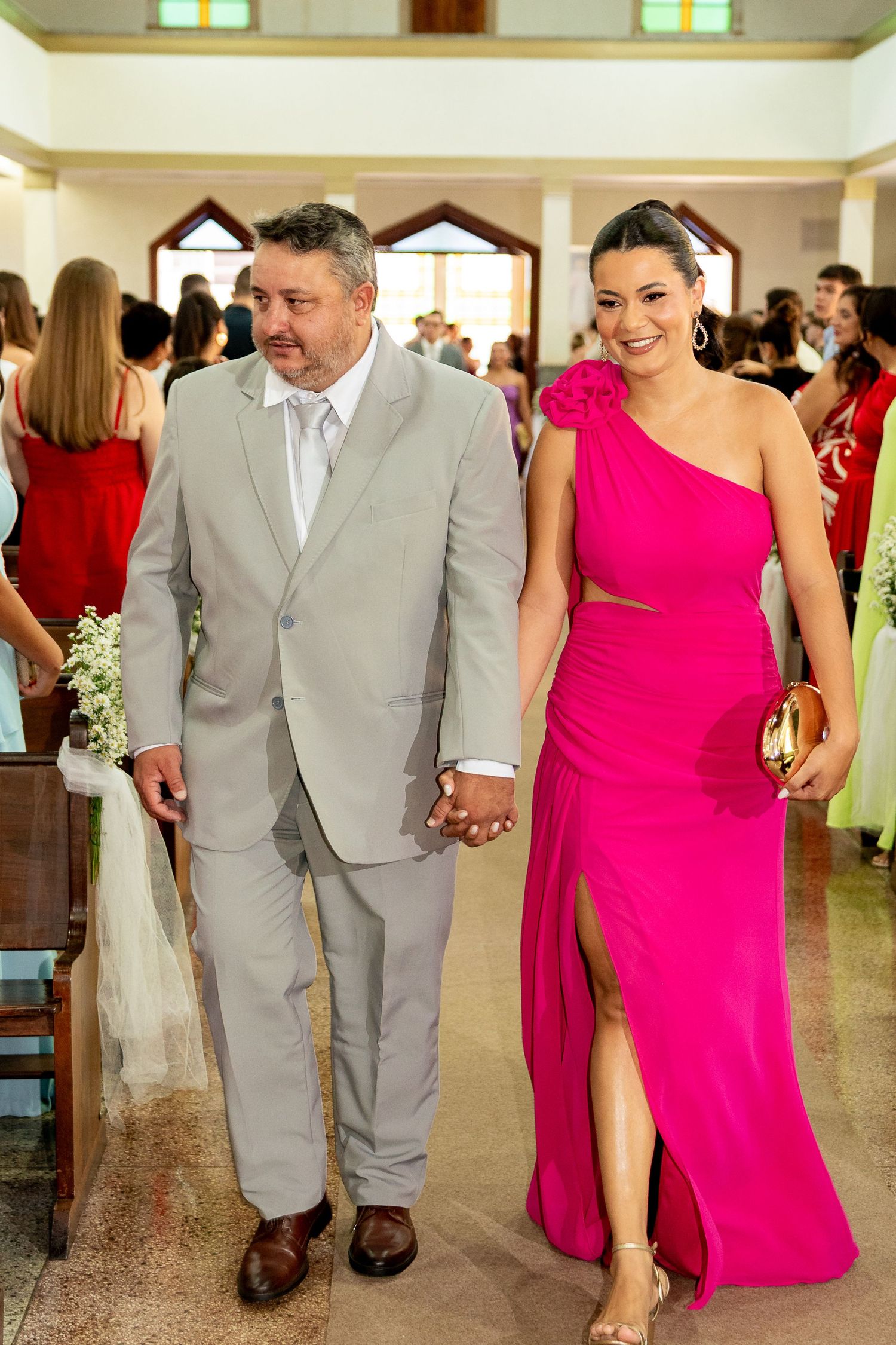 Couple walks down church aisle, man in gray suit, woman in pink one-shoulder gown, wedding ceremony.