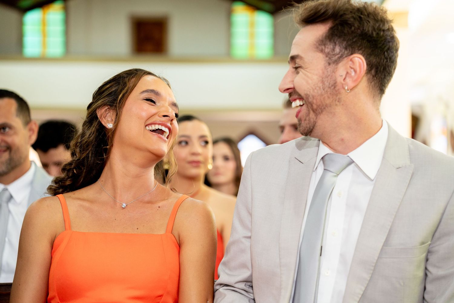A laughing couple in formal attire share a joyful moment at a wedding ceremony inside a church.