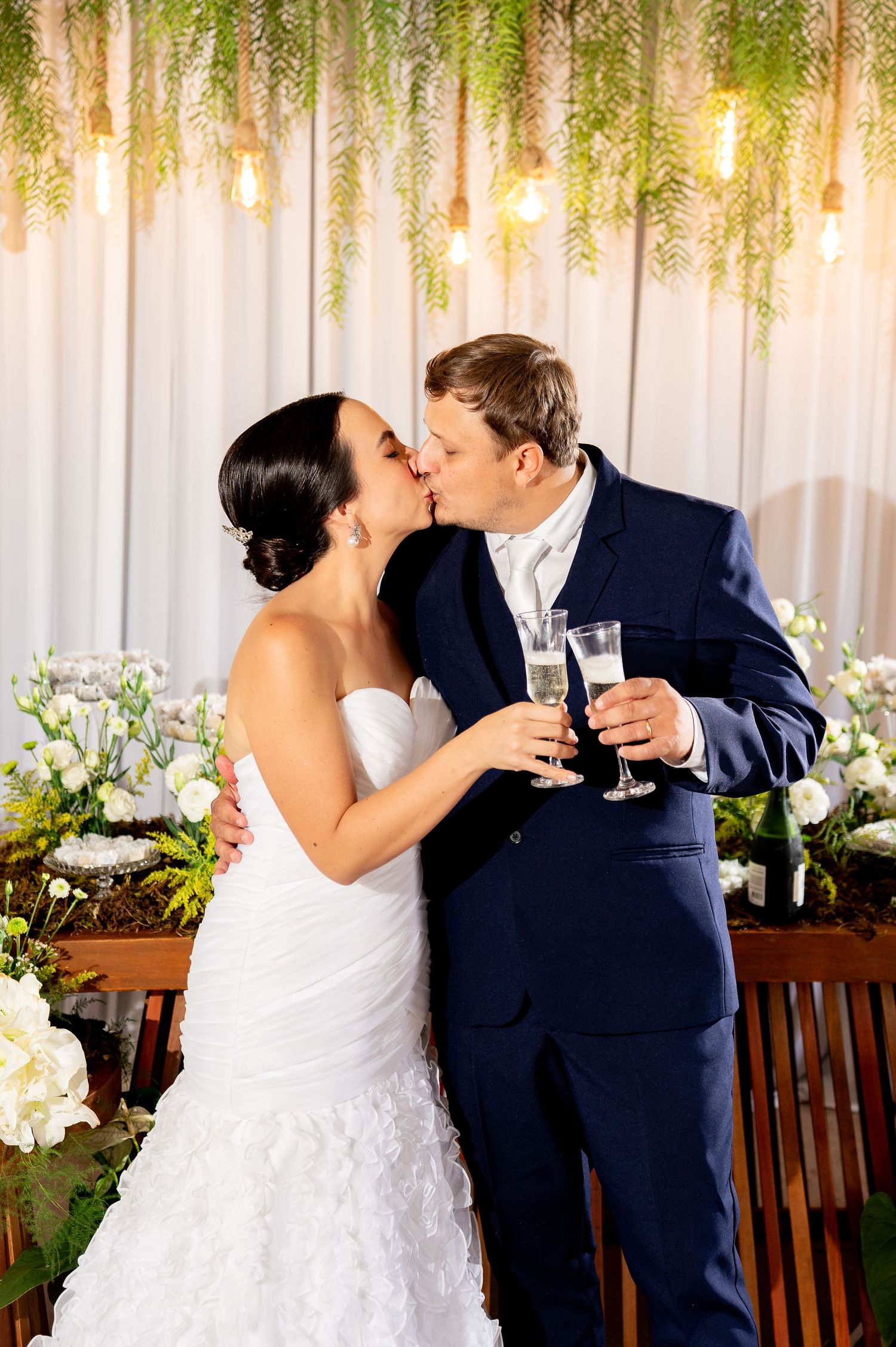 Bride and groom sharing a kiss while holding champagne glasses at their elegant wedding reception.