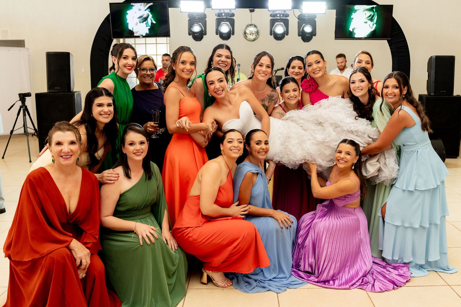 Bride poses with bridesmaids in colorful gowns at wedding reception venue.