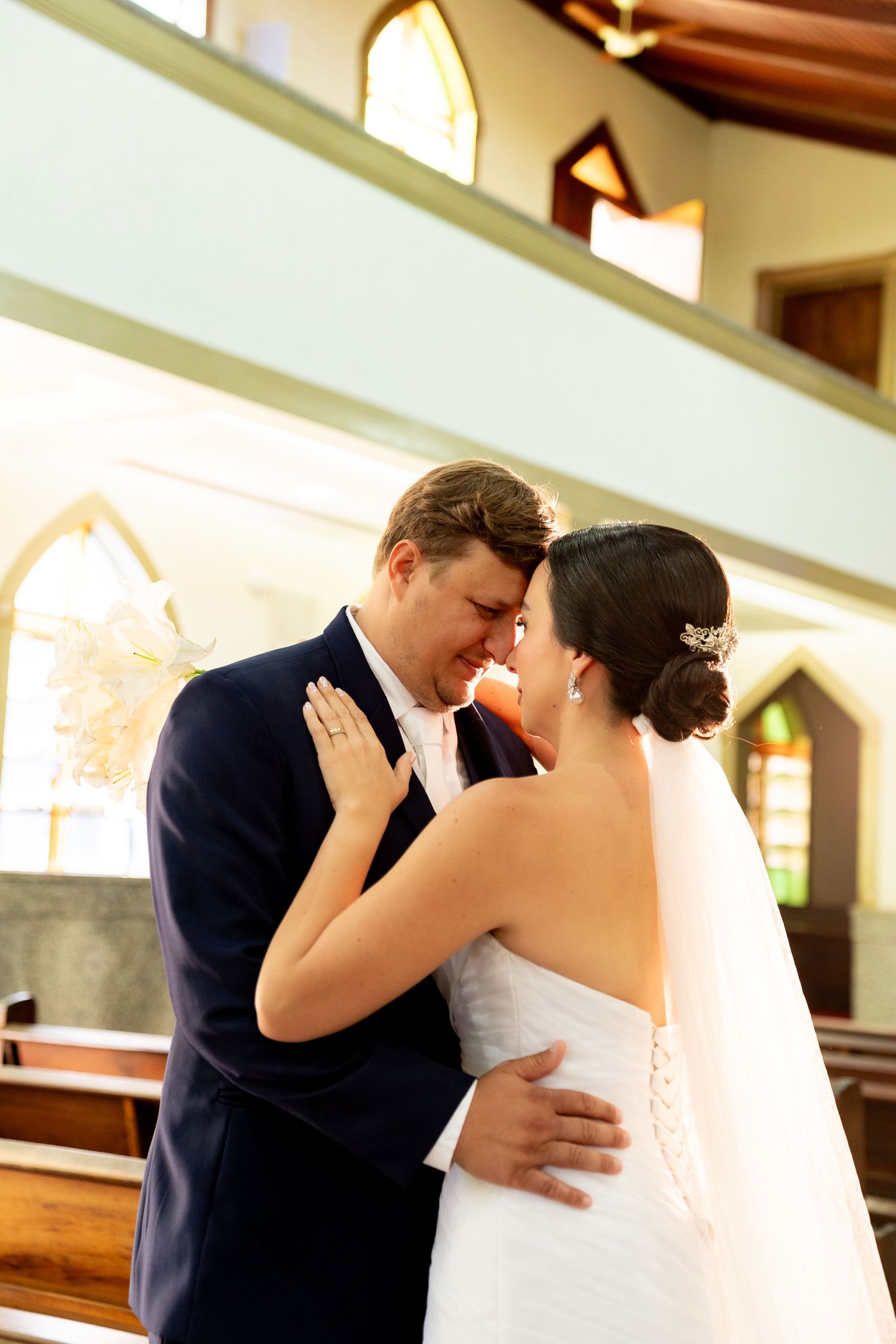 Bride and groom share an intimate moment at the altar inside a sunlit church on their wedding day.