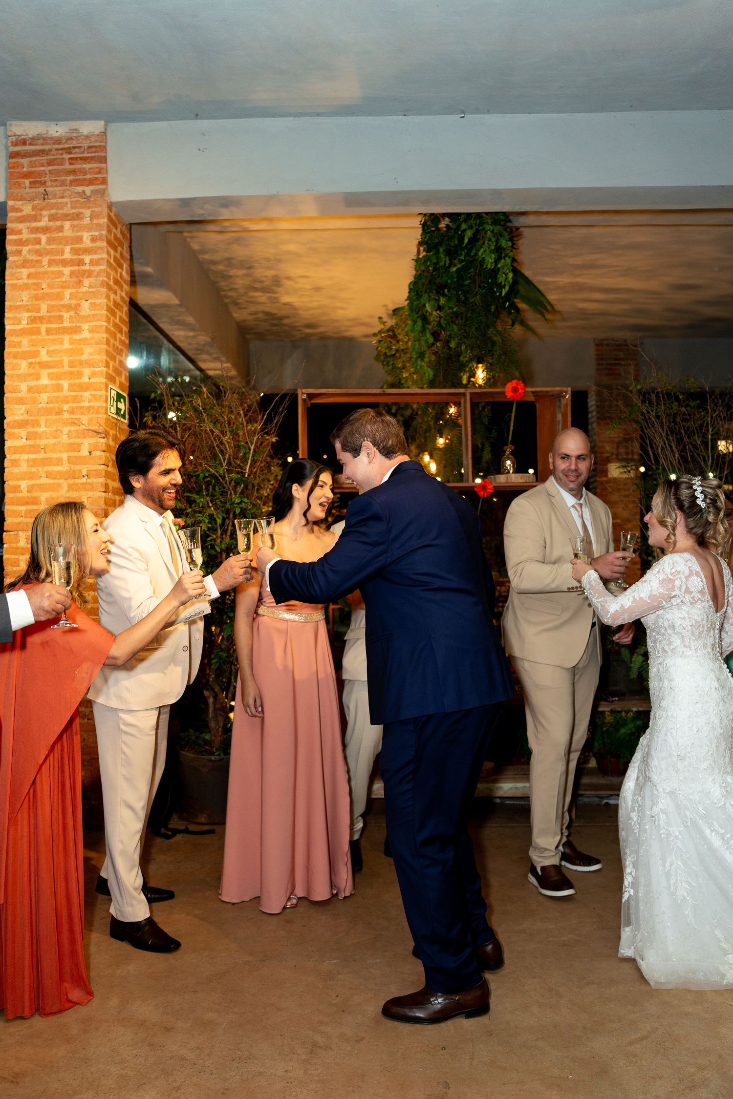 Wedding reception guests toasting with champagne, bride in white gown, bridesmaids in pink, groomsmen in navy and beige suits.
