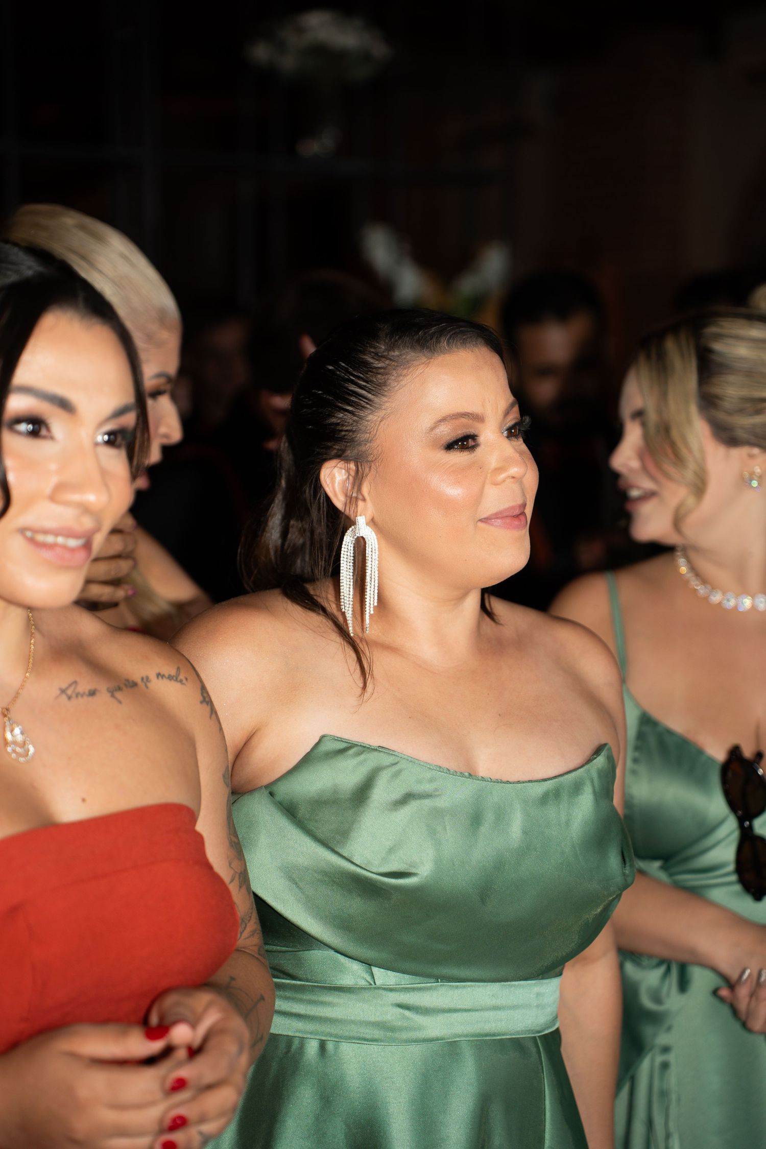 Women in elegant satin gowns in red and green at a formal event, smiling and socializing.