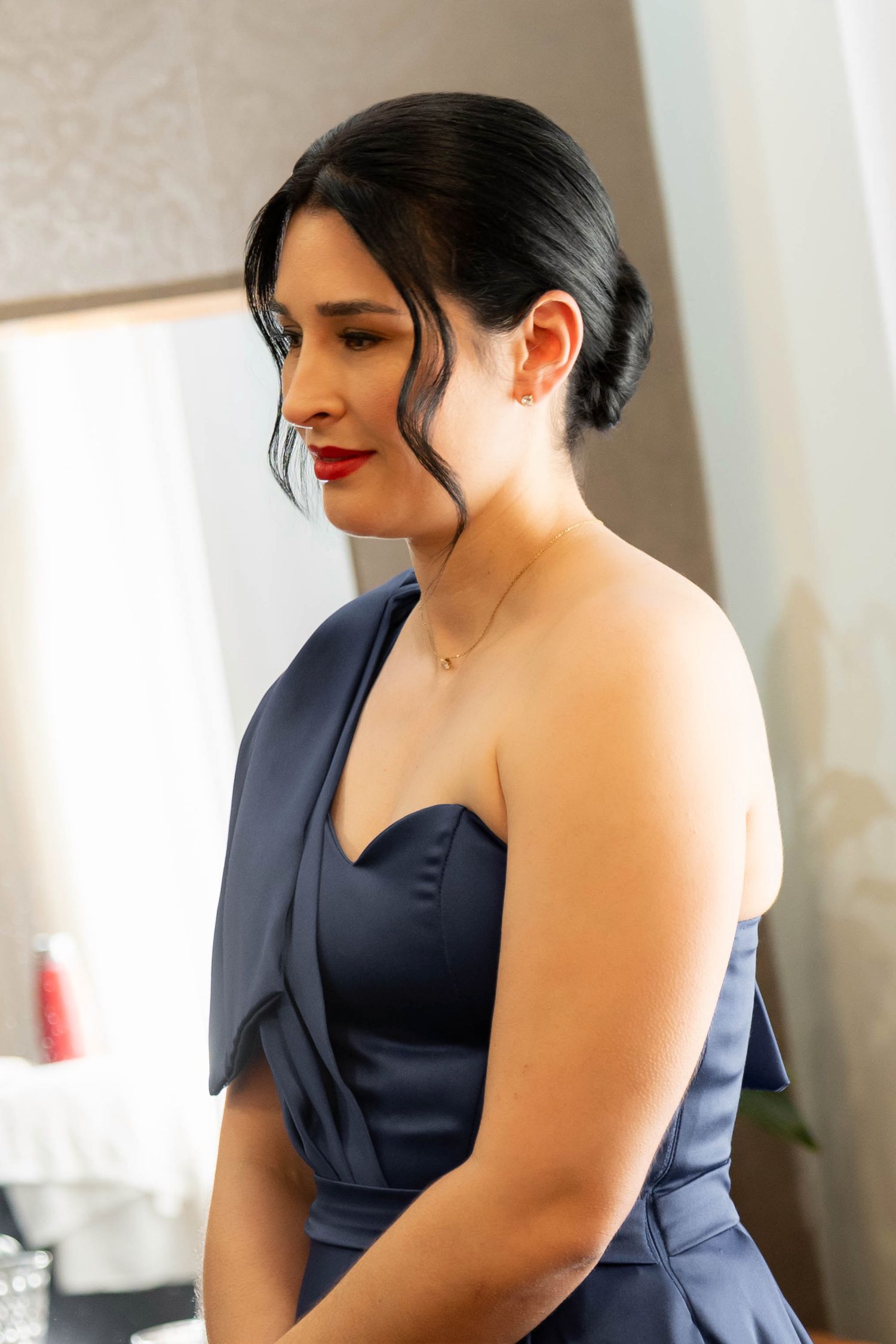 Elegant woman in navy blue strapless gown with red lips and updo hairstyle, wearing a delicate gold necklace.