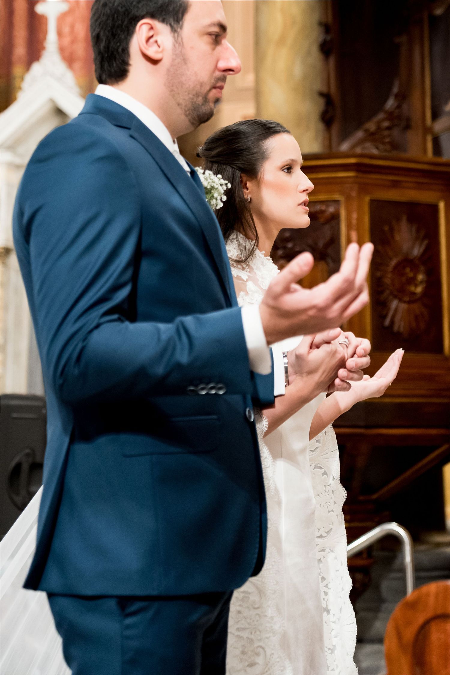 Bride and groom praying together at church altar during wedding ceremony, wearing white lace dress and navy blue suit.