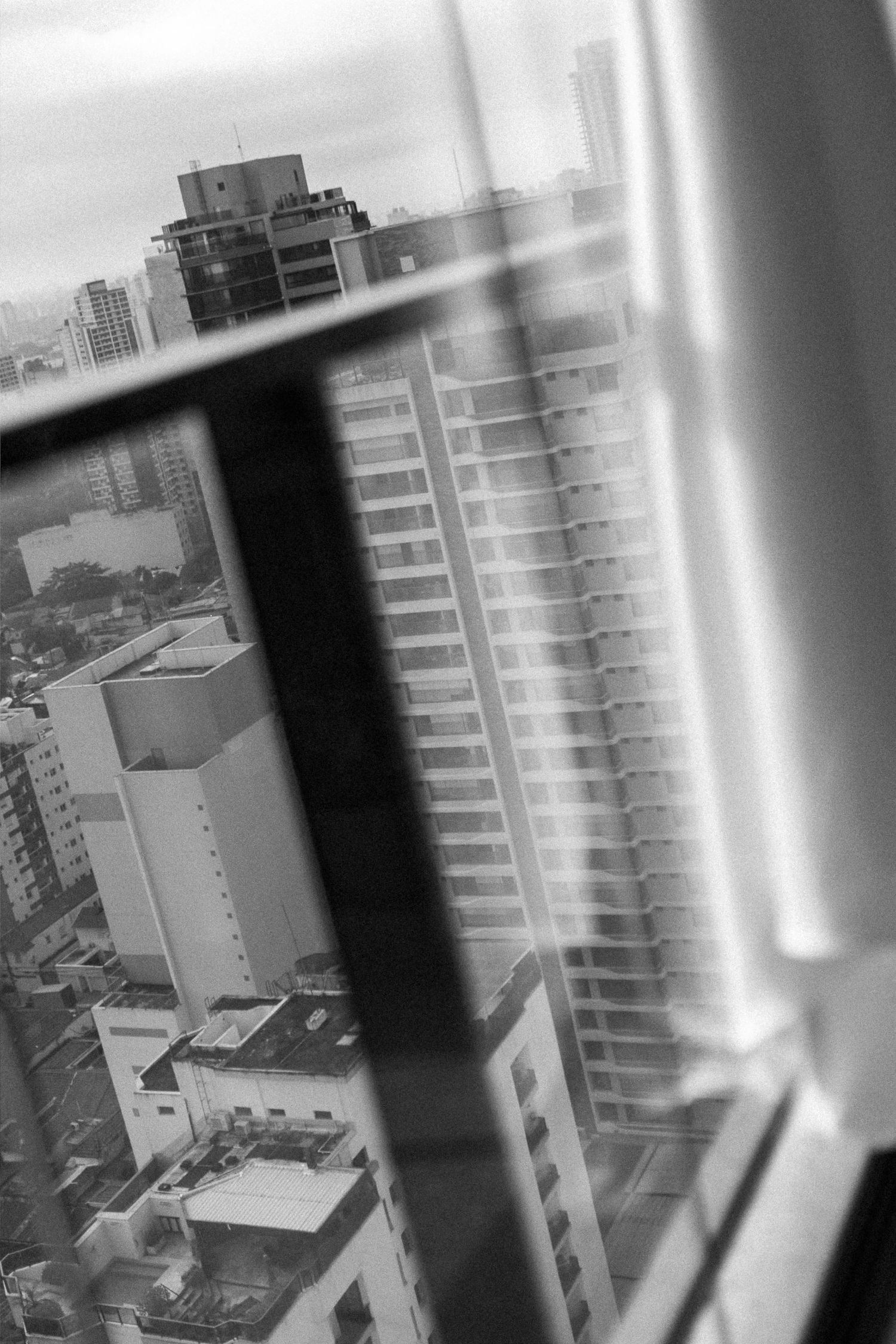 Black and white aerial city view through a window, showing dense urban skyline with tall buildings.