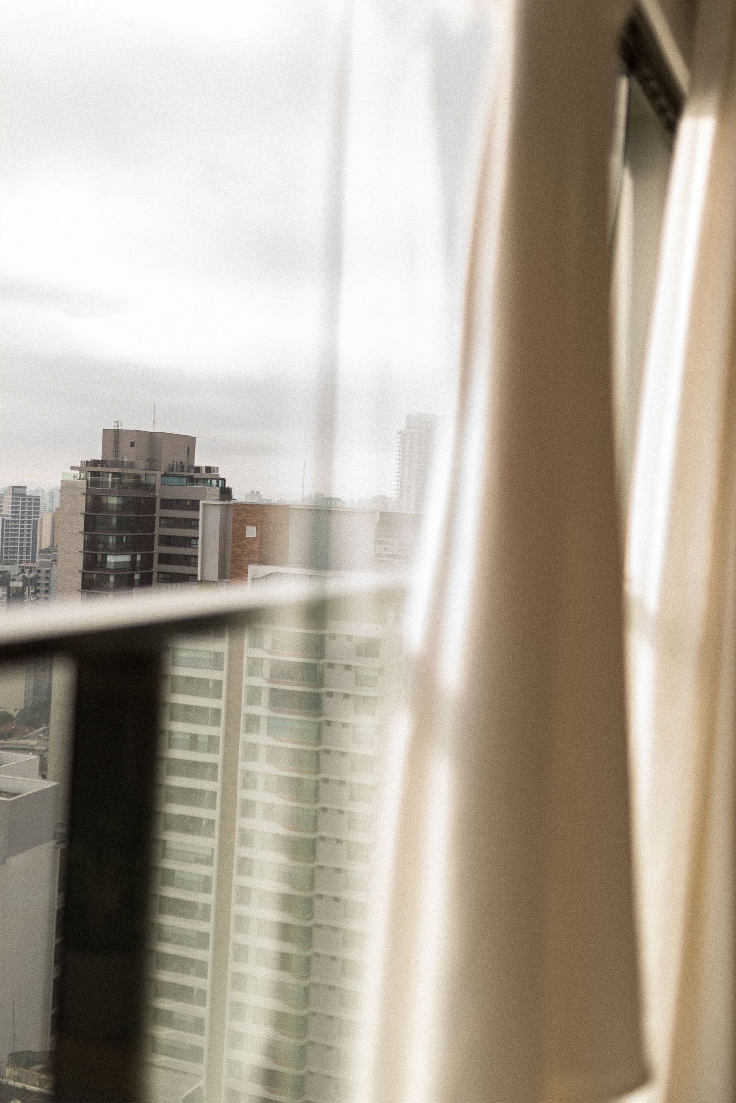 City skyline viewed through a window with sheer curtains on an overcast day.