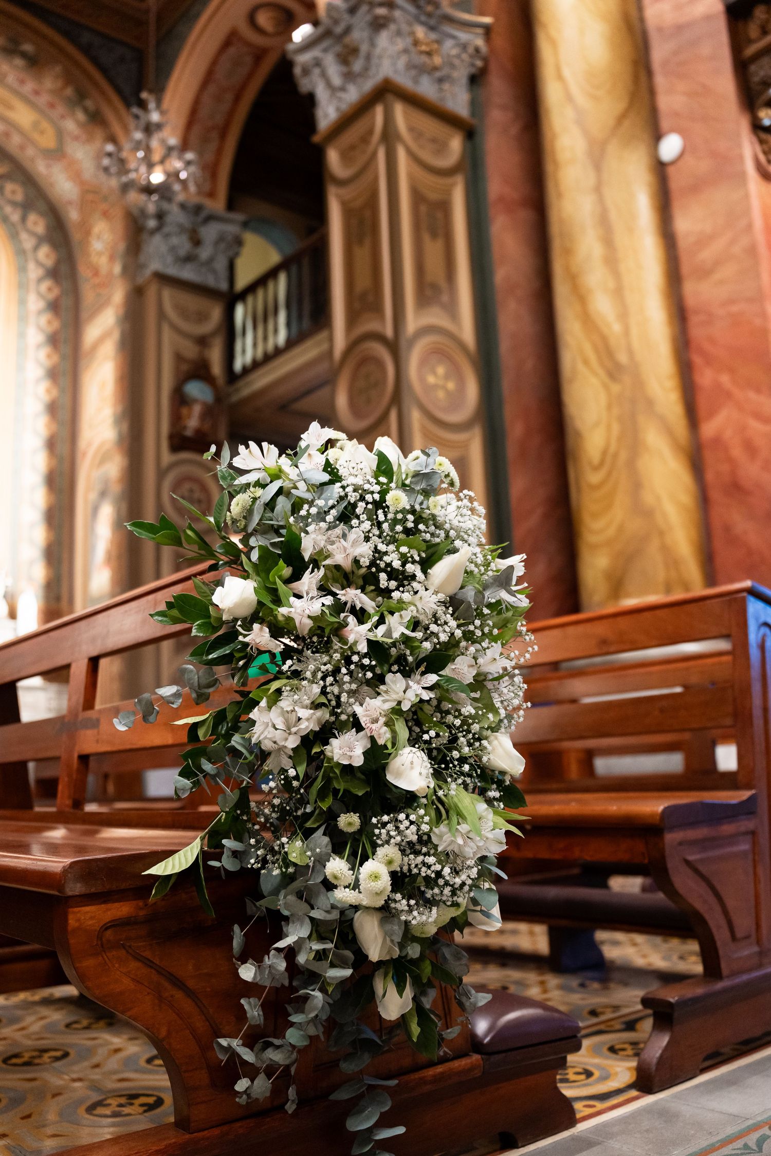 White floral arrangement decorating wooden church pews during a wedding ceremony in an ornate chapel.